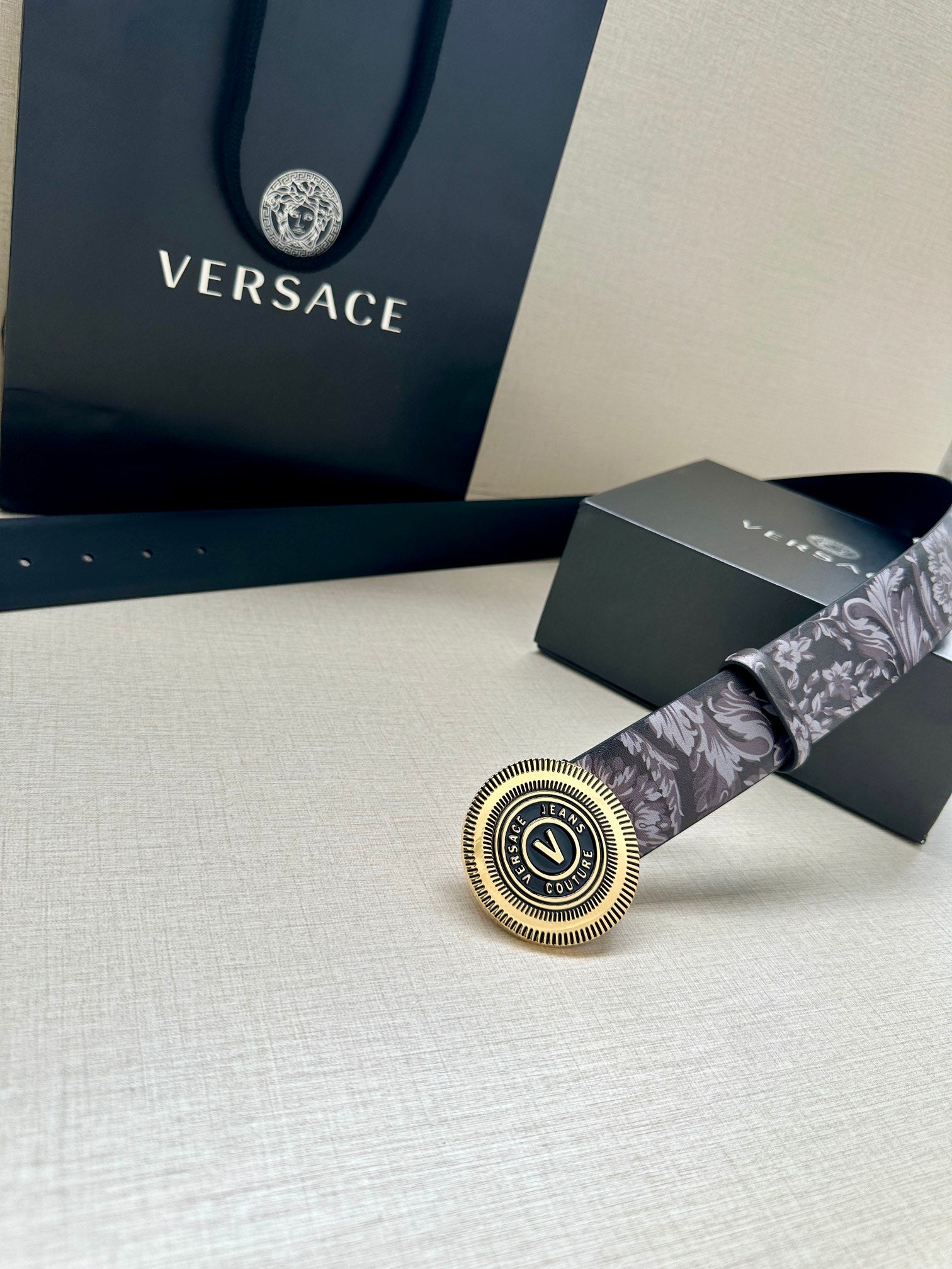 Versace belt buckle close-up on gray floral strap, circular gold emblem