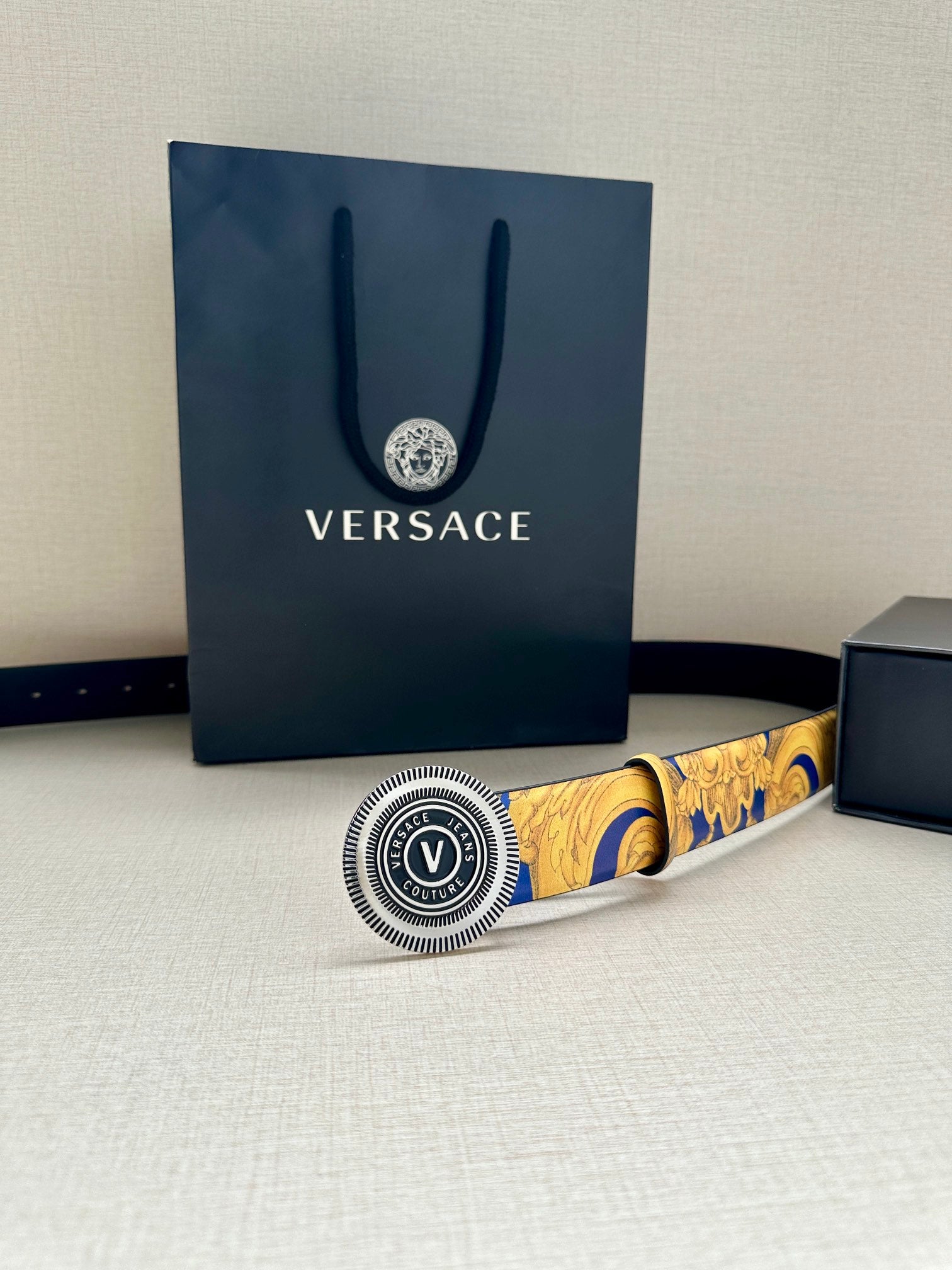 Belt with gold-and-blue baroque print and round Versace logo buckle, across surface.