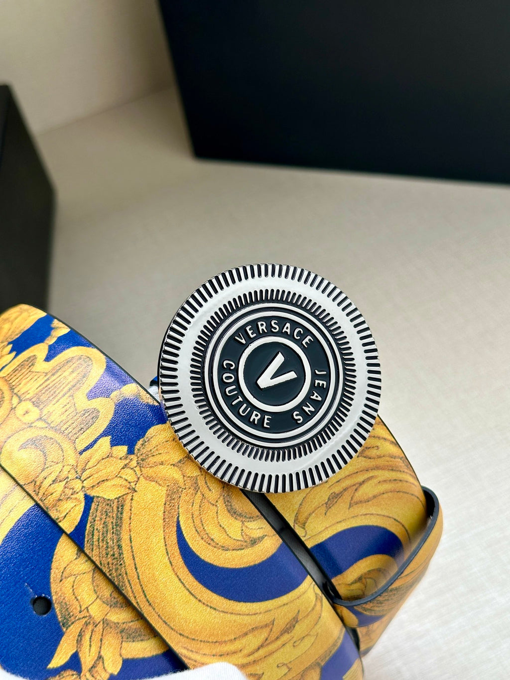 Round Versace logo belt buckle on gold-and-blue baroque strap.