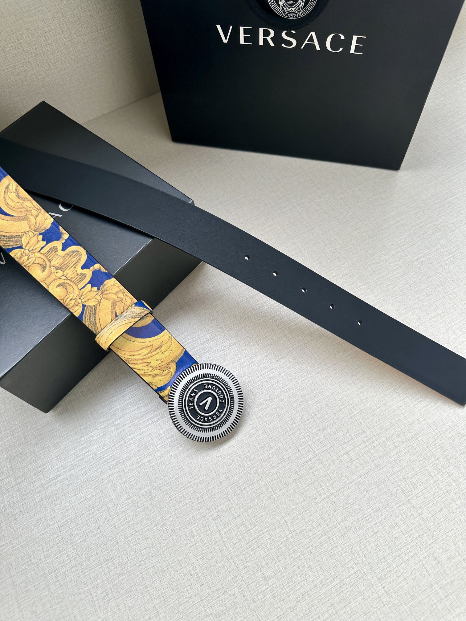 Belt with gold-and-blue baroque print and round Versace logo buckle, lying flat.
