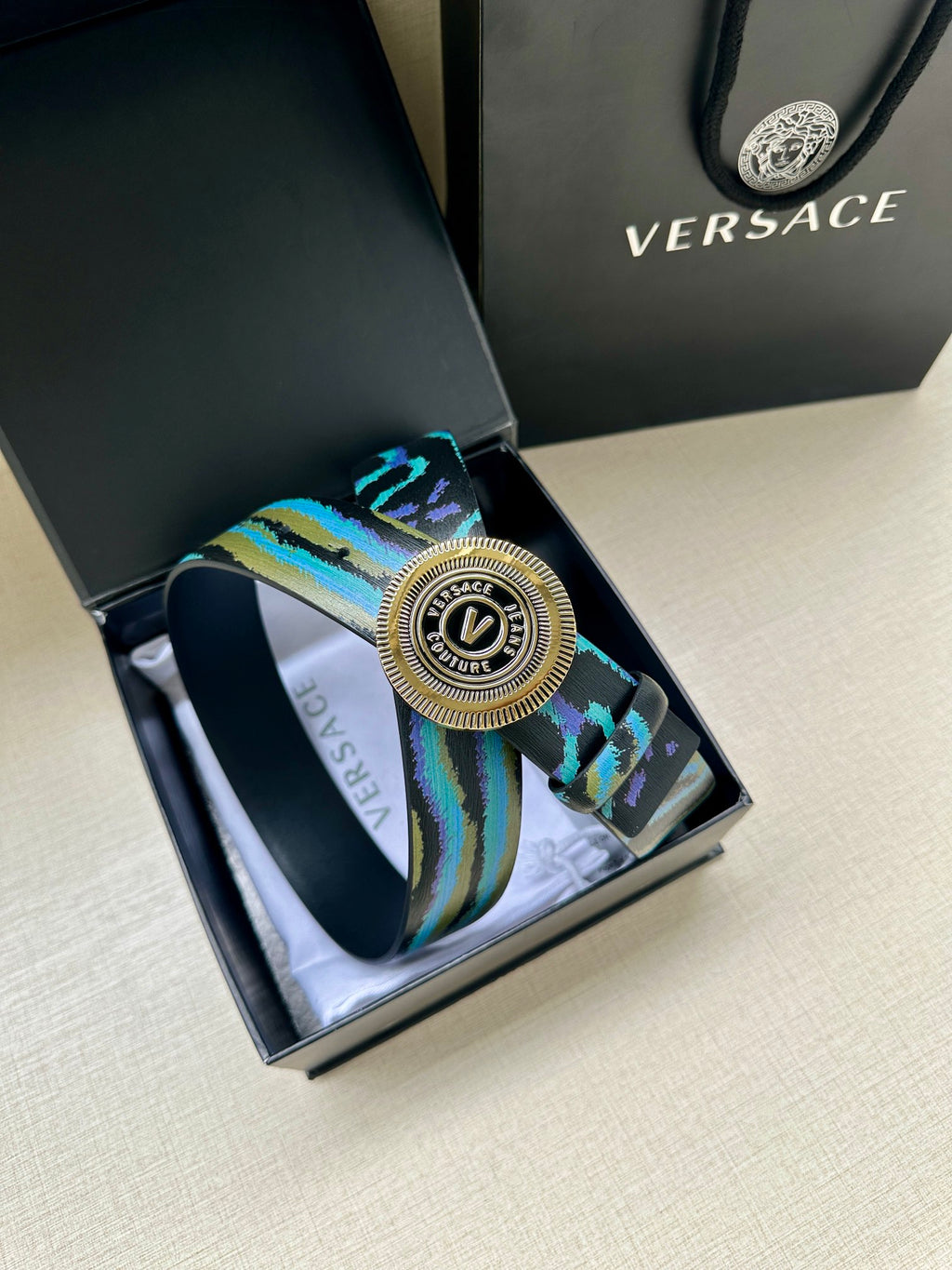 Versace belt detail: teal-blue patterned strap with circular silver buckle centerpiece