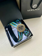 Versace belt detail: teal-blue patterned strap with circular silver buckle centerpiece