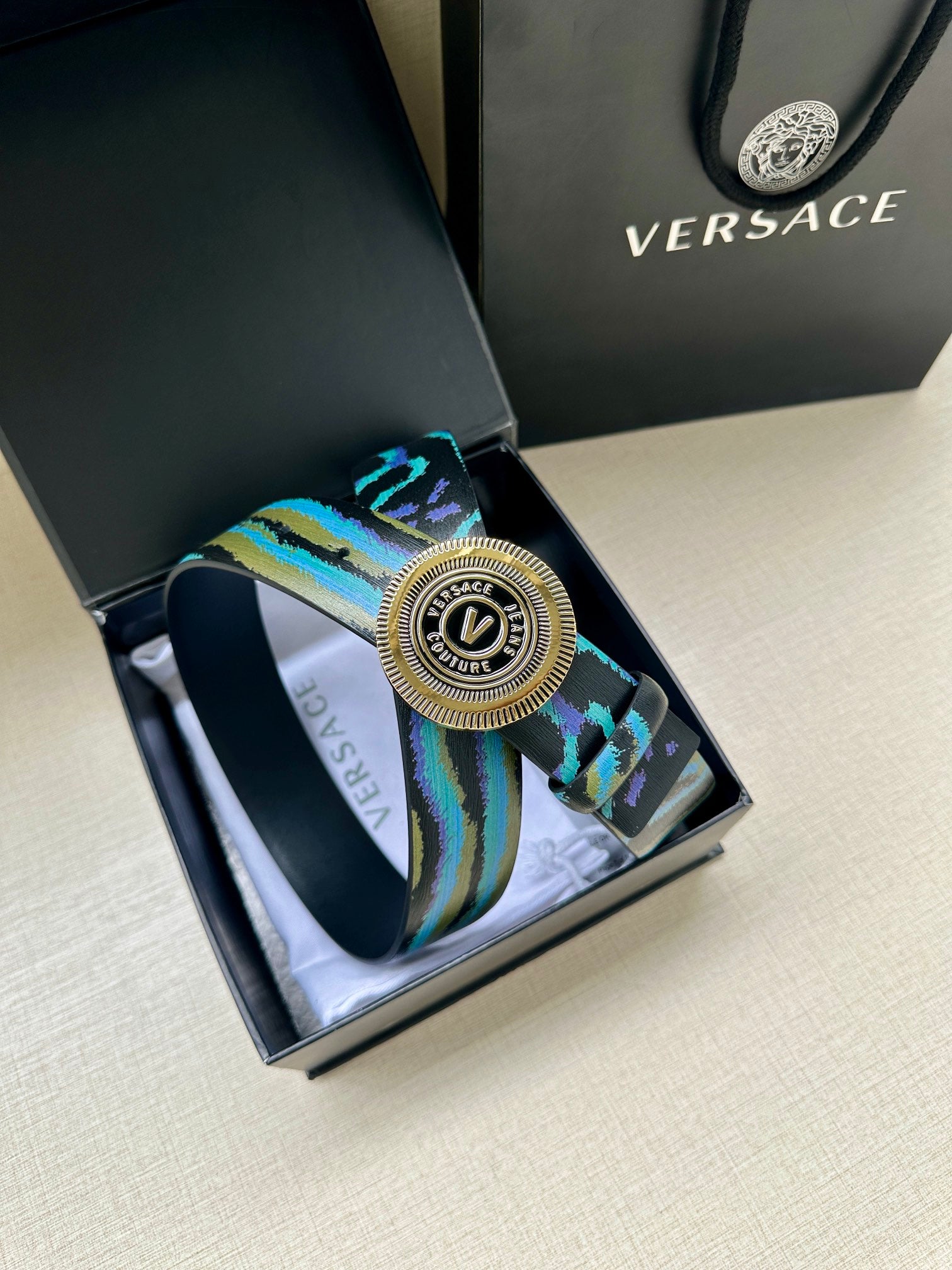 Versace belt detail: teal-blue patterned strap with circular silver buckle centerpiece