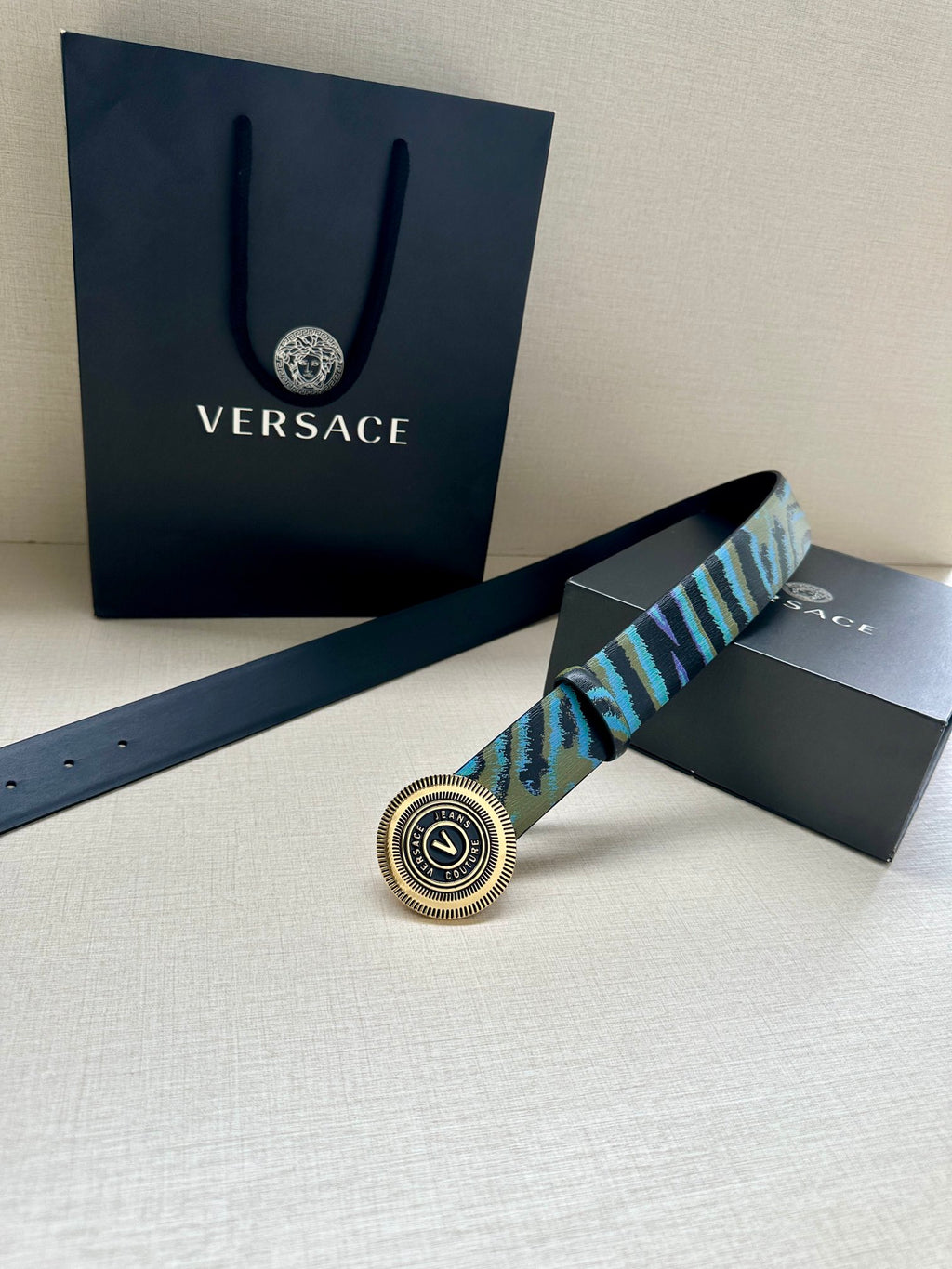 Versace belt laid flat: teal-blue patterned strap with round silver logo buckle