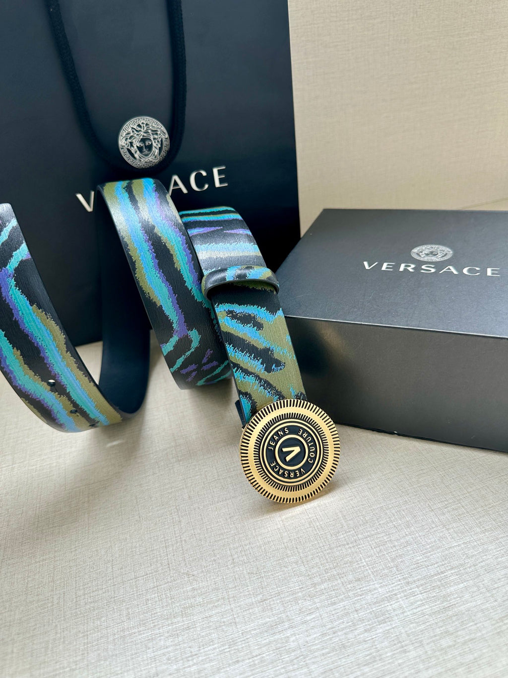 Versace belt buckle close-up on teal-blue patterned strap with round silver medallion