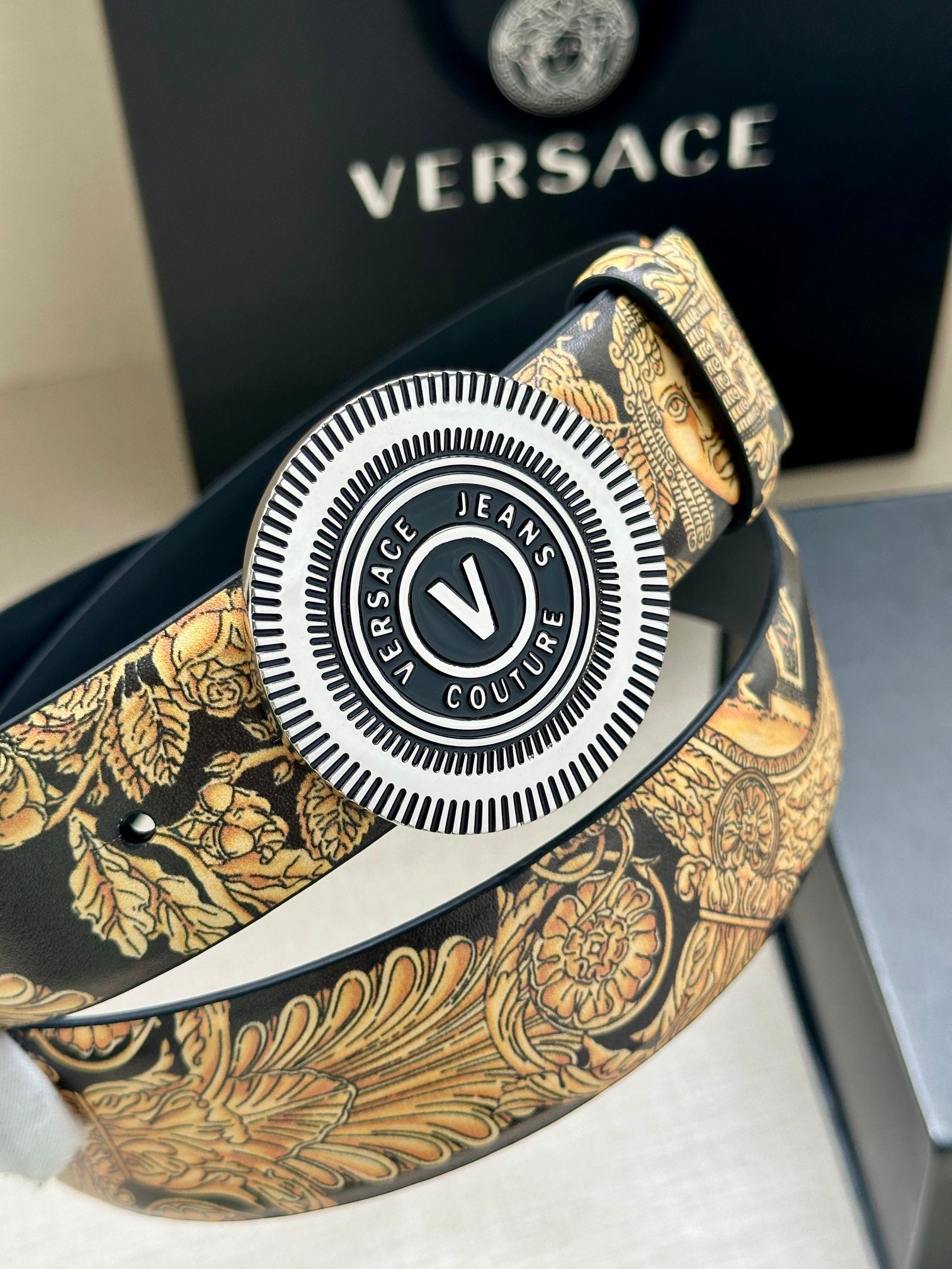 Versace belt buckle close-up: round V logo with textured gold baroque strap