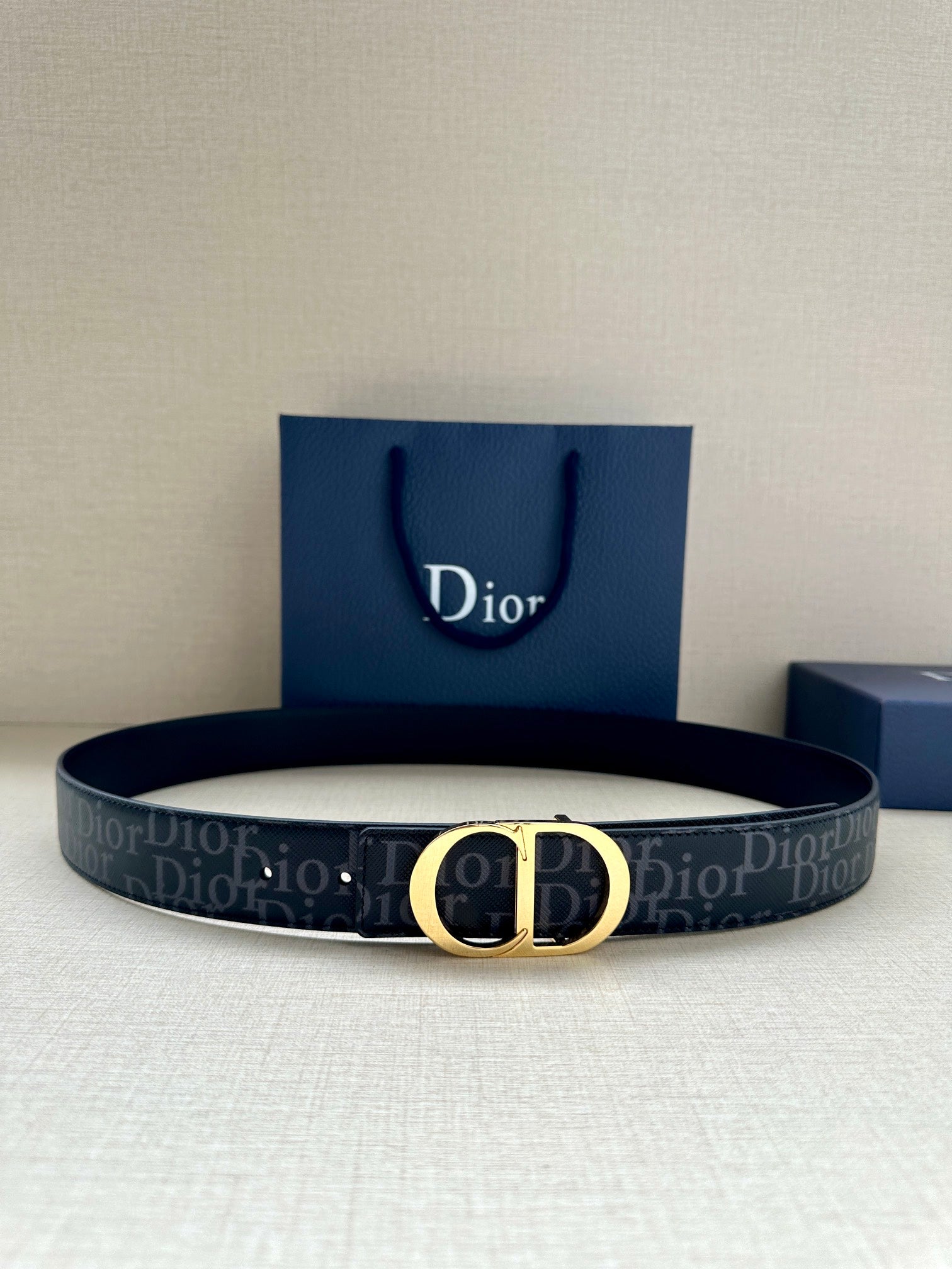 Dior belt with dark monogram strap and gold CD buckle, shown with gift bag