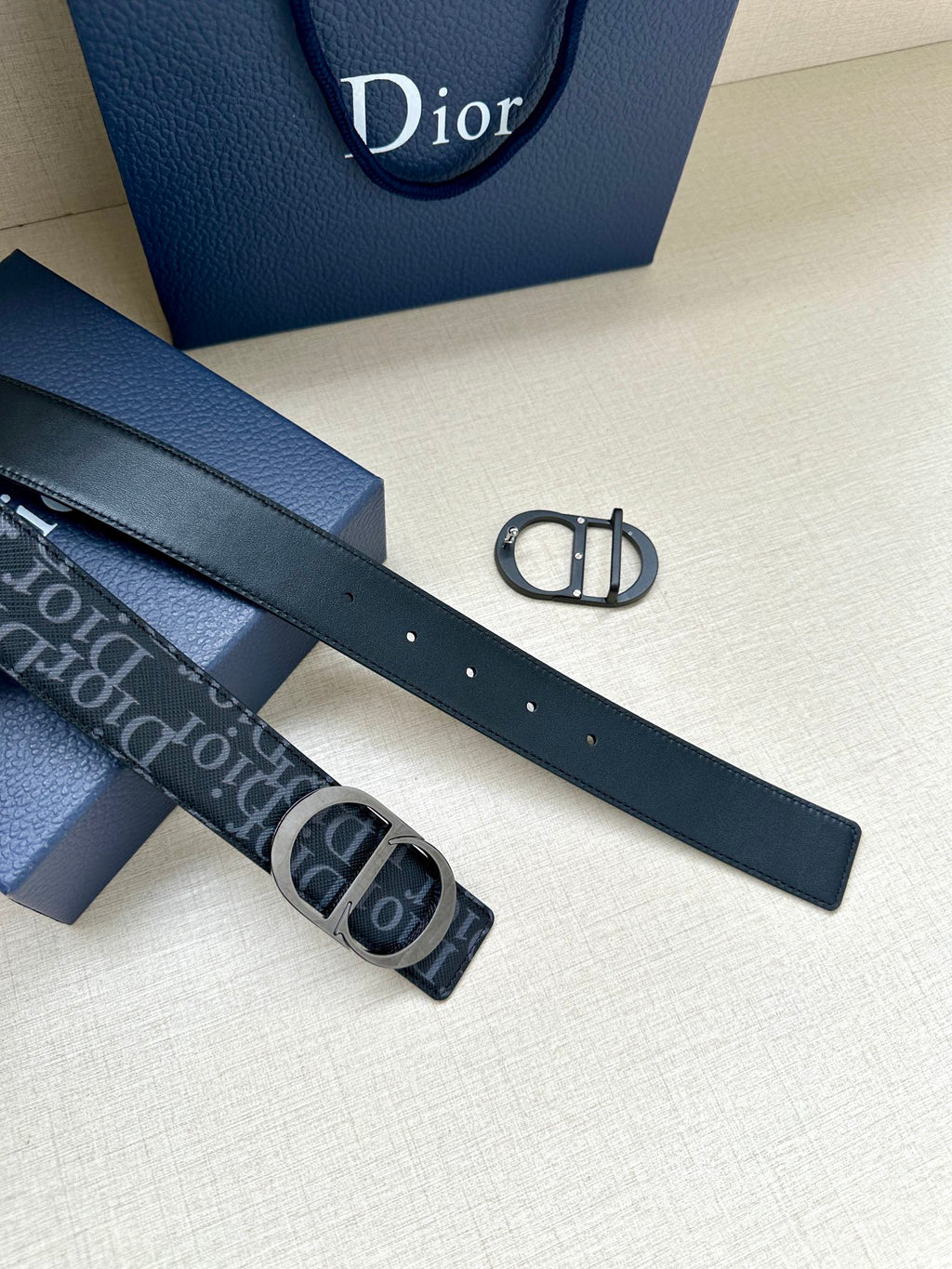 Dior belt strap with punched holes and smooth dark leather, beside patterned belt