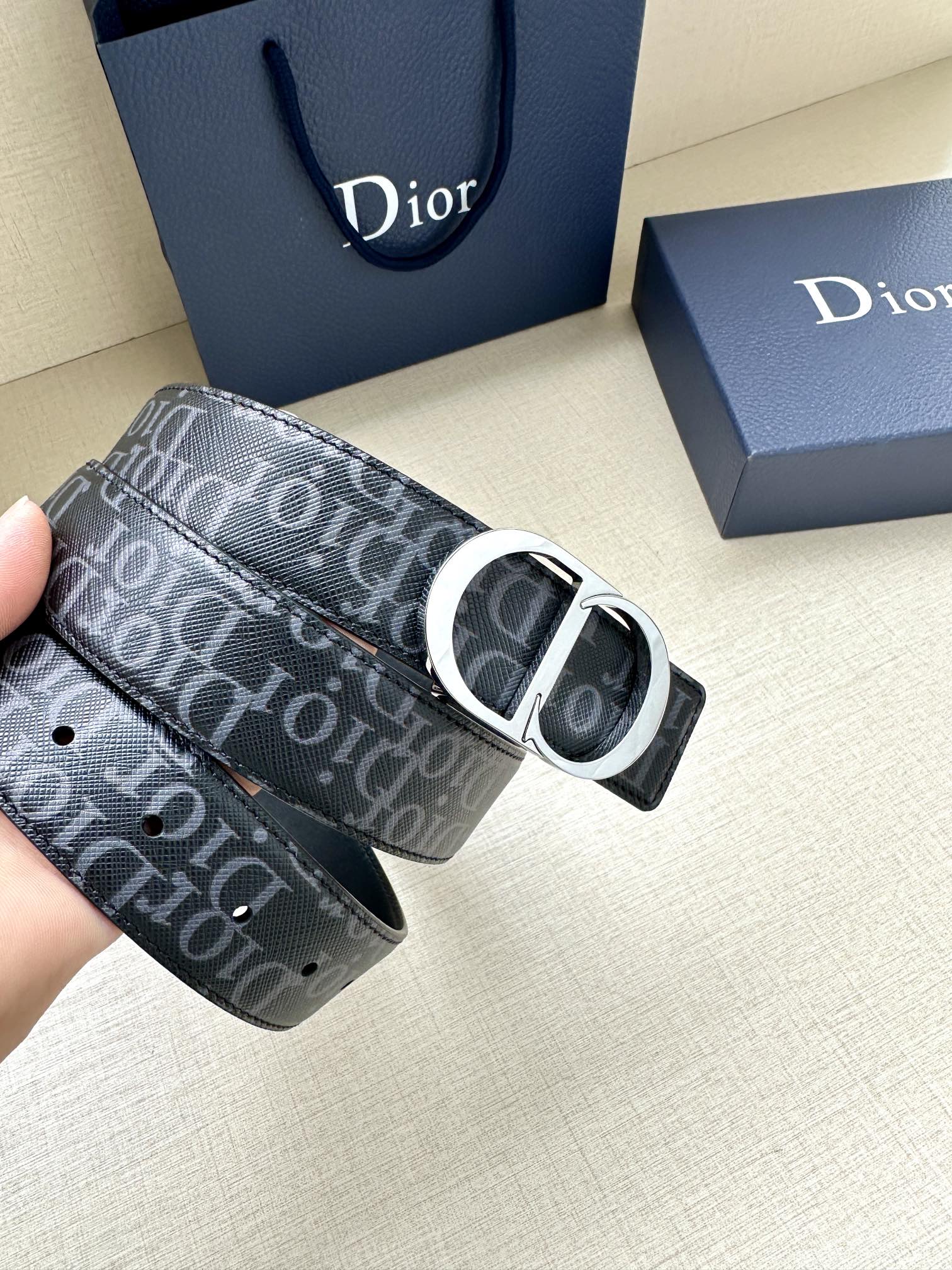 Dior belt with dark monogram strap and silver buckle, held in hand