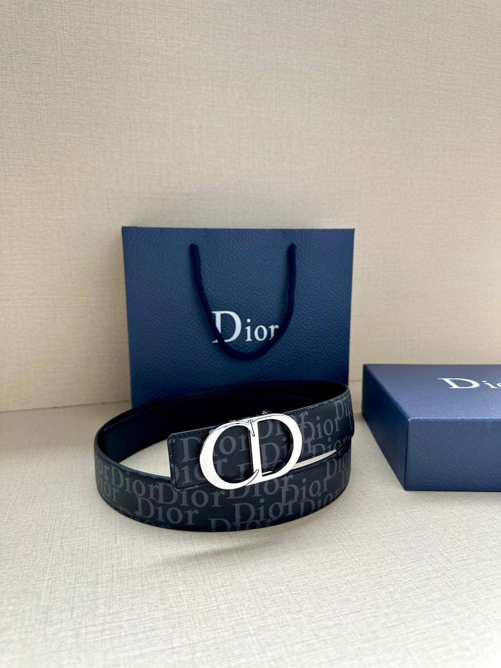 Dior belt with dark monogram strap and black CD buckle, resting on box