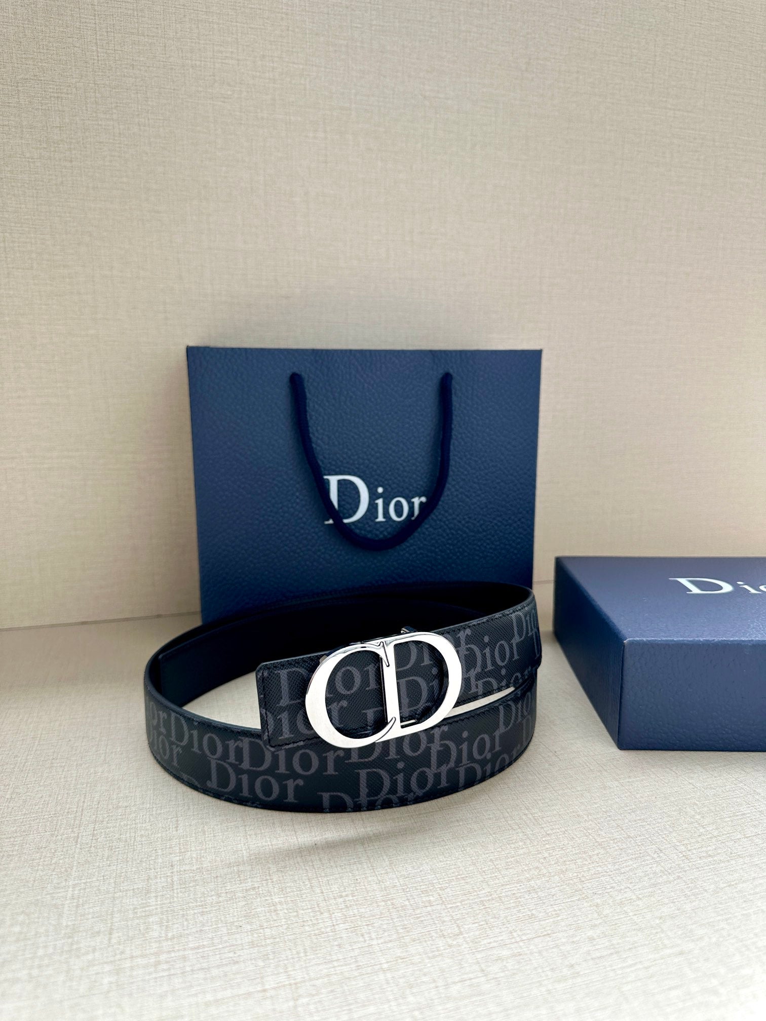 Dior belt with dark monogram strap and black CD buckle, resting on box