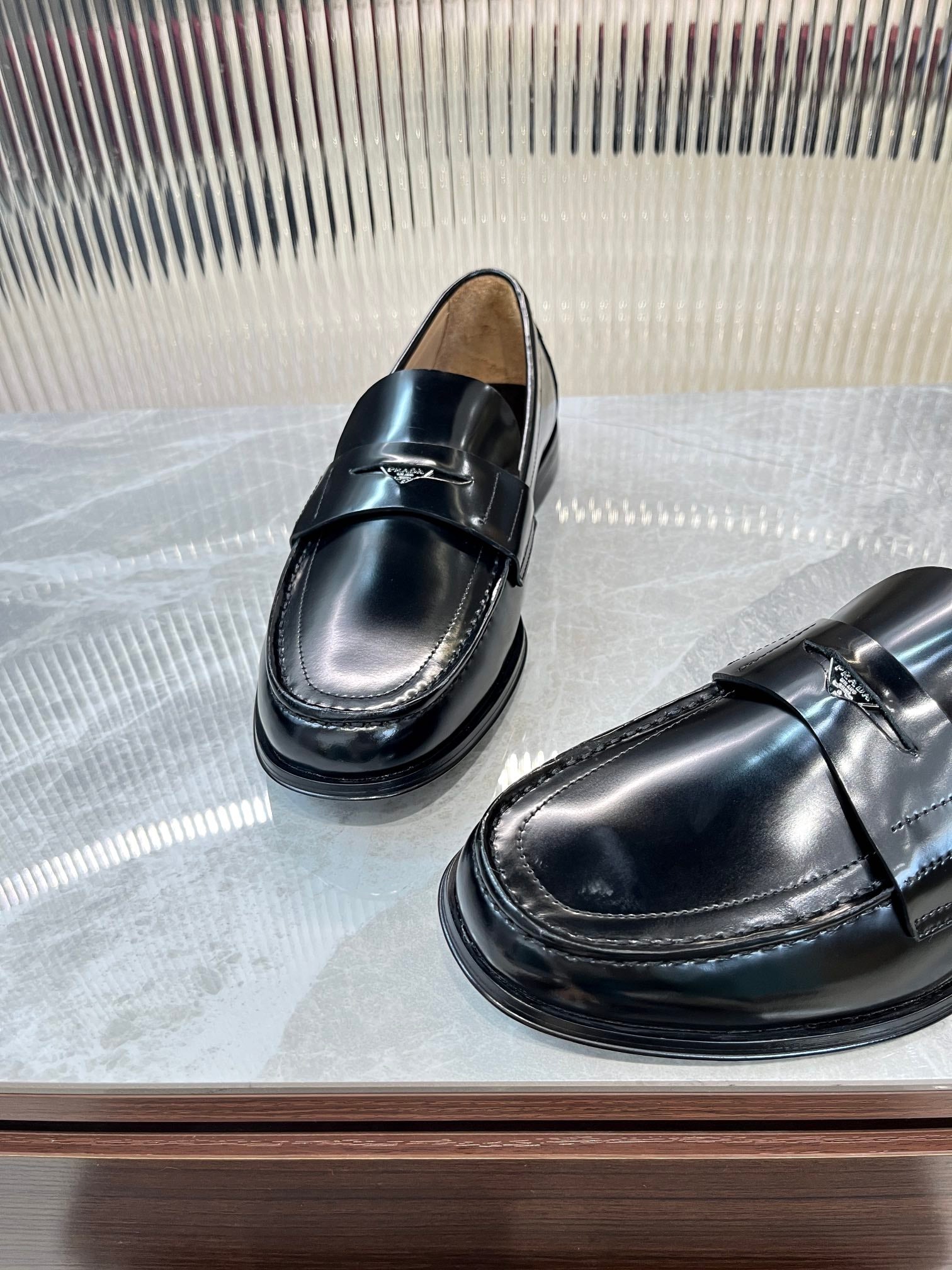 Prada unisex black leather loafers, angled front view showing metal strap detail.
