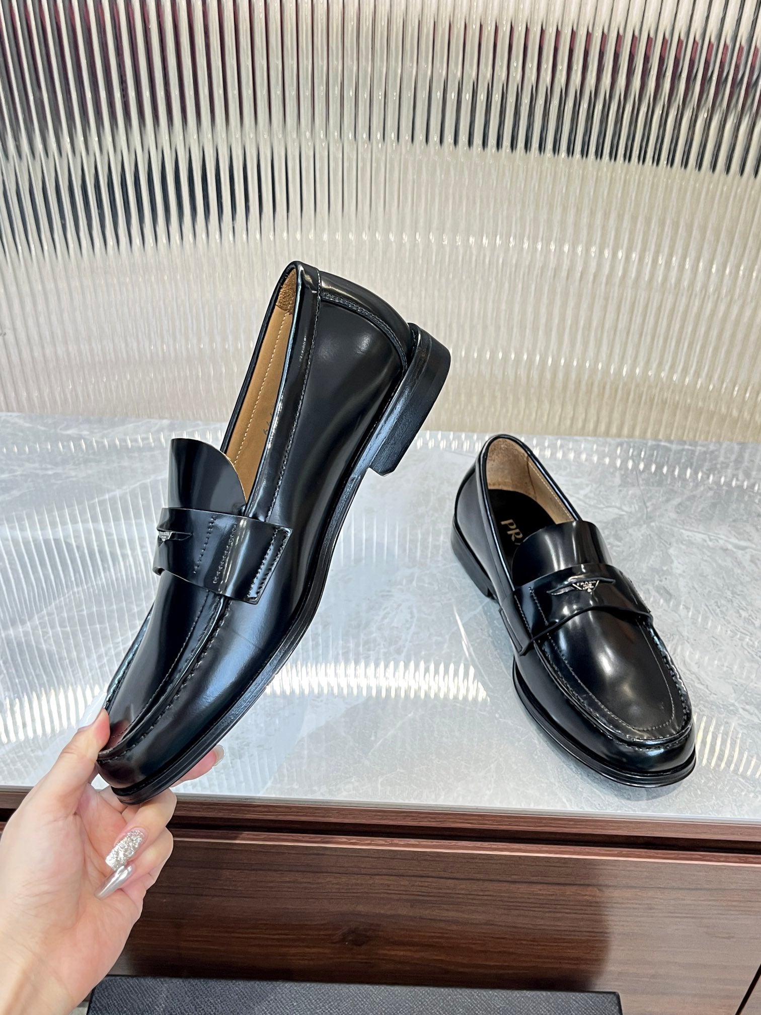 Prada unisex black leather loafers, one held by hand, metal strap across front.