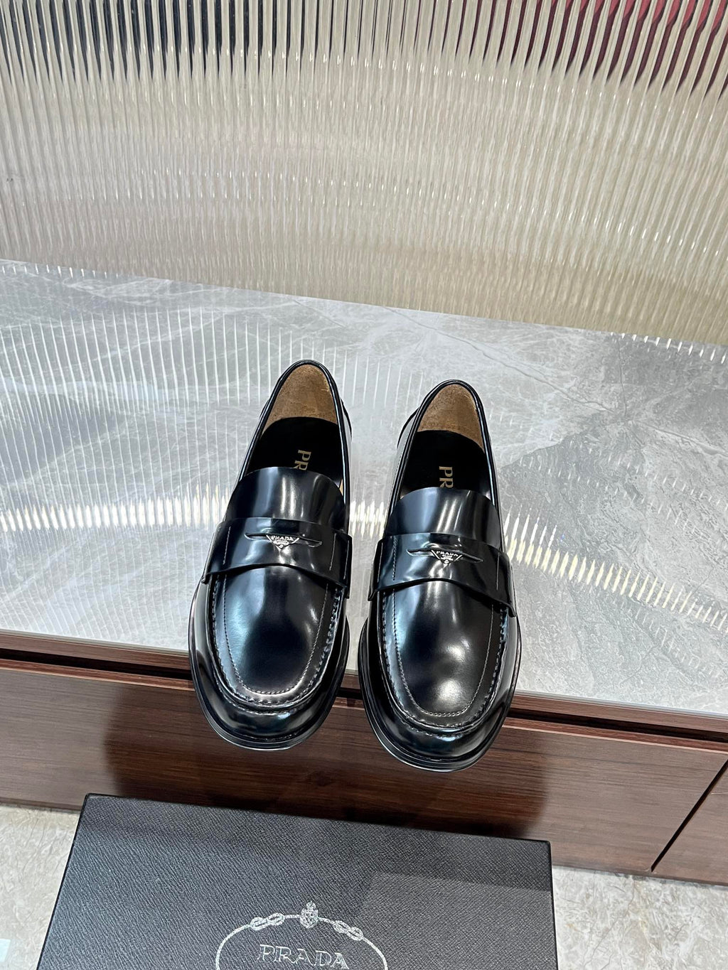 Prada unisex black leather loafer with metal strap across the vamp, polished finish.