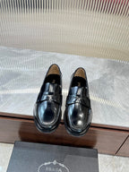 Prada unisex black leather loafer with metal strap across the vamp, polished finish.