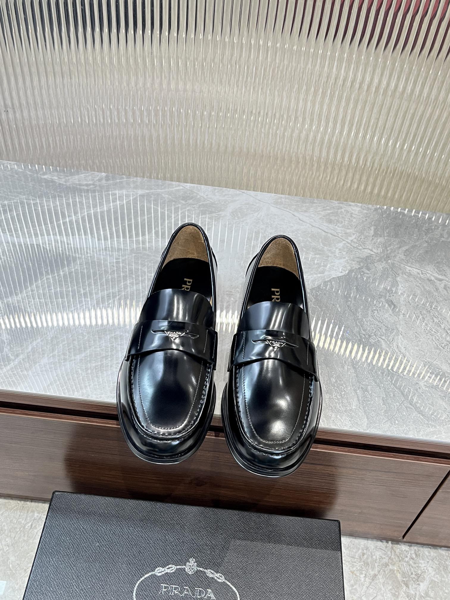 Prada unisex black leather loafer with metal strap across the vamp, polished finish.
