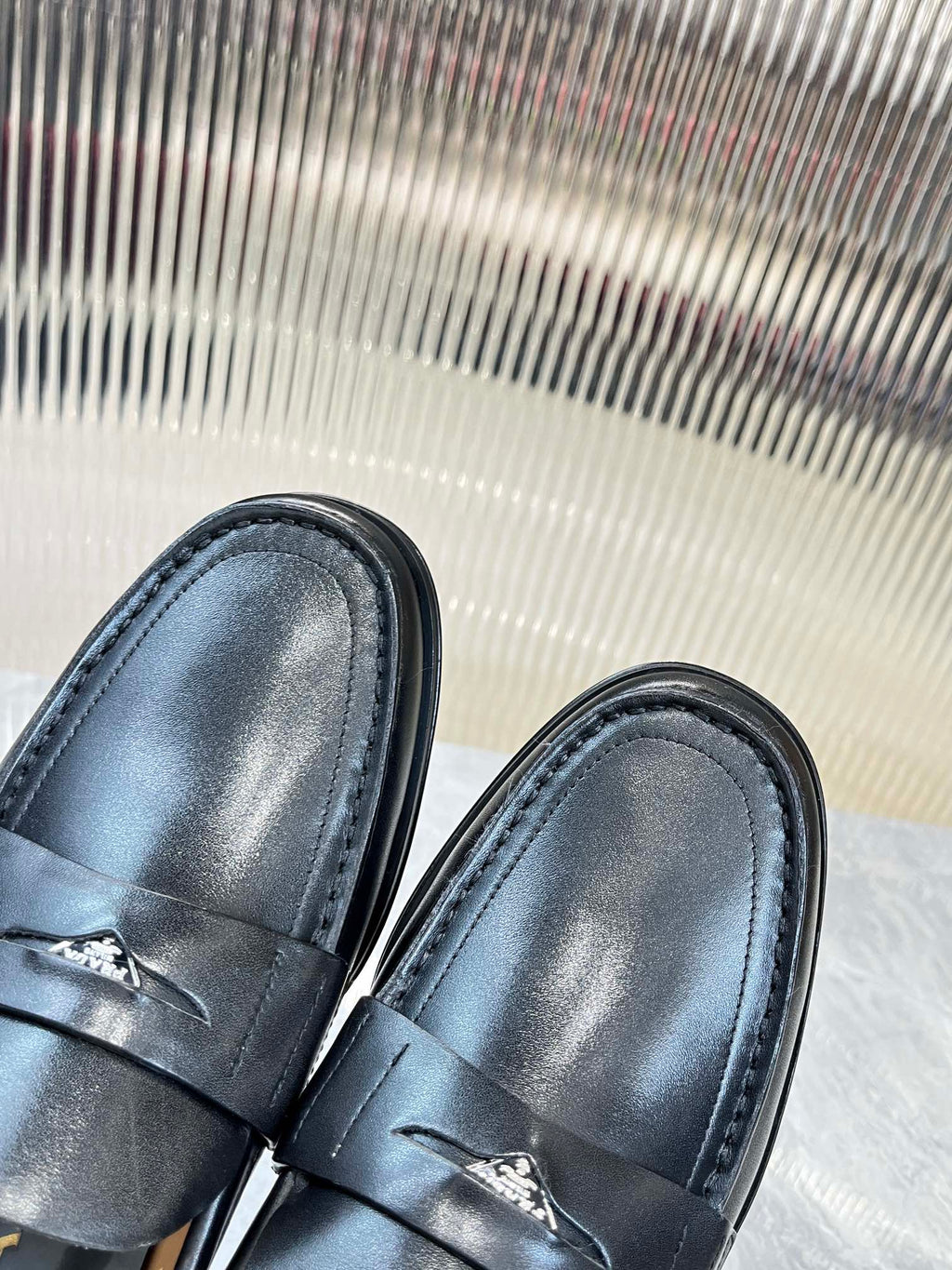 Prada leather loafers toe close-up, dark finish with strap stitching and emblem