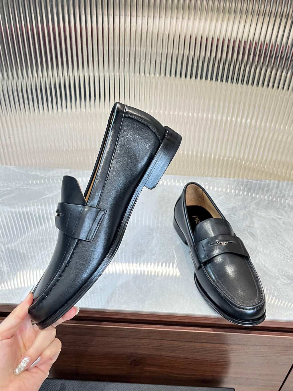 Prada unisex leather loafers, dark color, held pair shot with strap across vamp