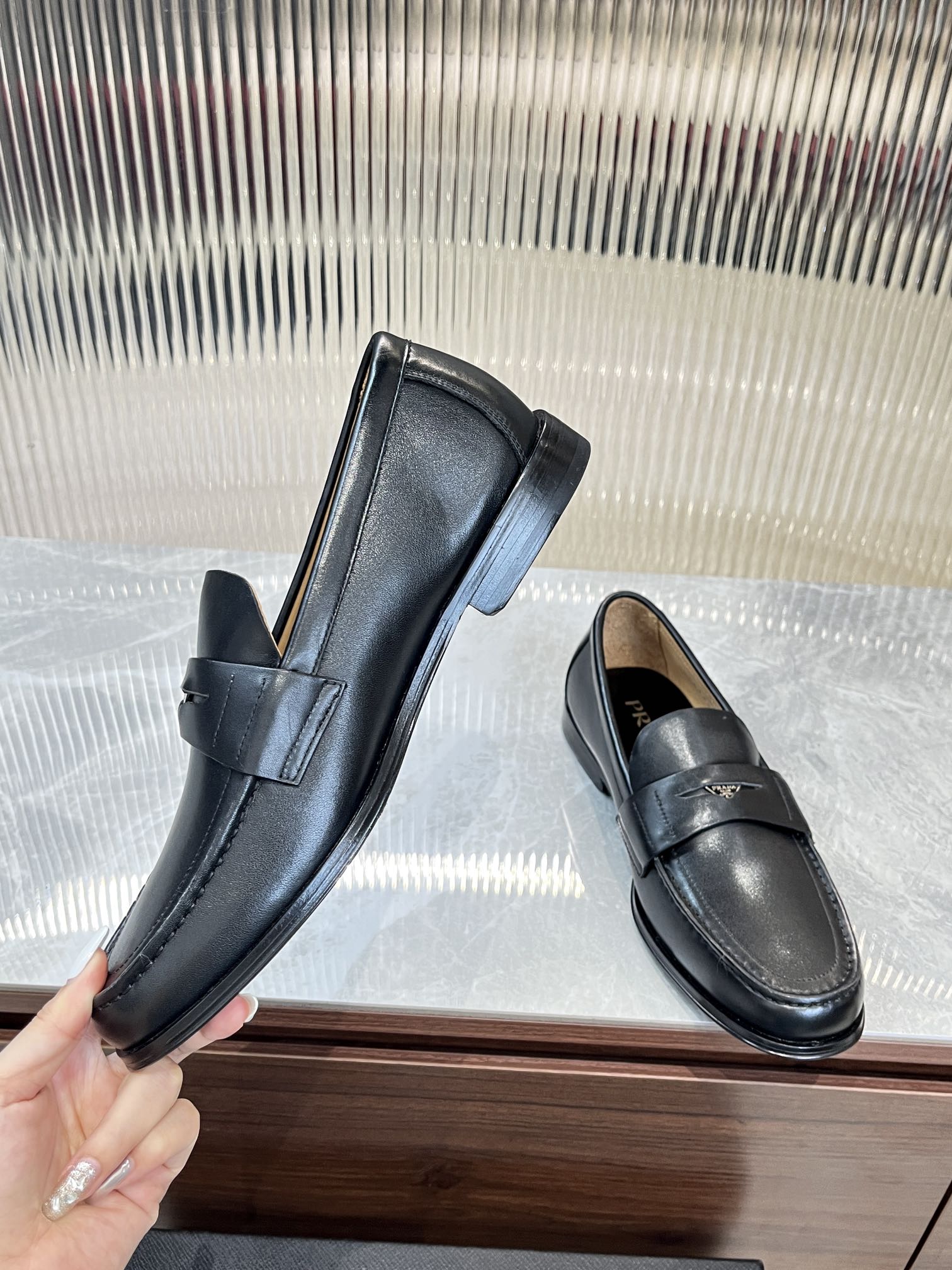 Prada unisex leather loafers, dark color, held pair shot with strap across vamp