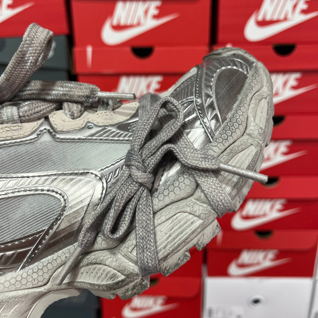 Silver metallic sneaker side view with lace-up closure, textured overlays, and thick midsole.