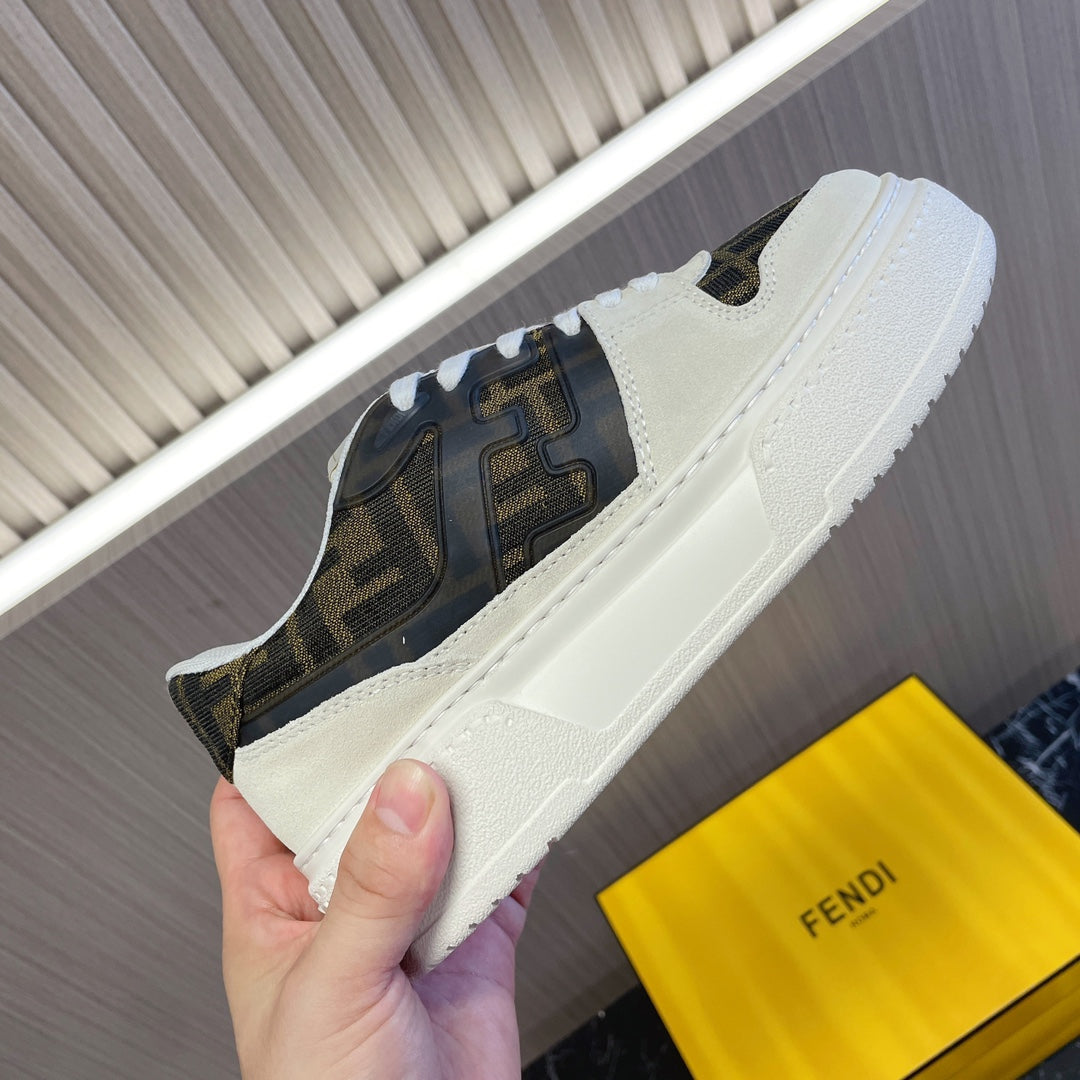 Low-top sneaker held in hand, cream upper with dark logo paneling and white sole.