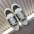 Low-top sneakers with white laces, dark monogram panels, and cream leather trim.