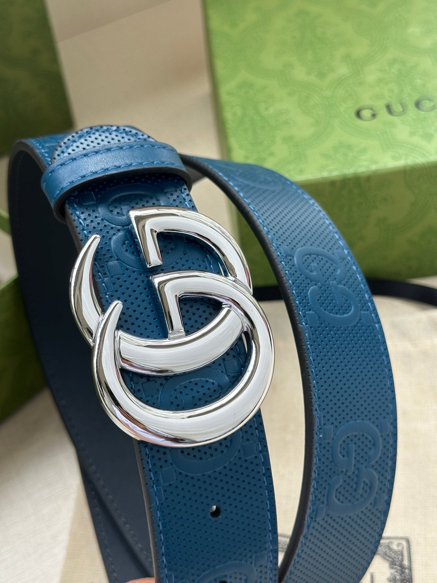 Blue leather belt with silver-tone GG buckle, close-up of textured strap and clasp