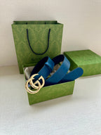 Blue leather belt with gold-tone GG buckle, laid across green shopping bags