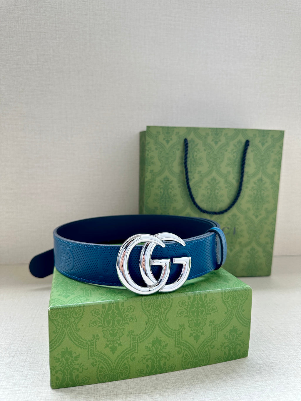 Blue leather belt with silver-tone GG buckle, posed on a green gift box