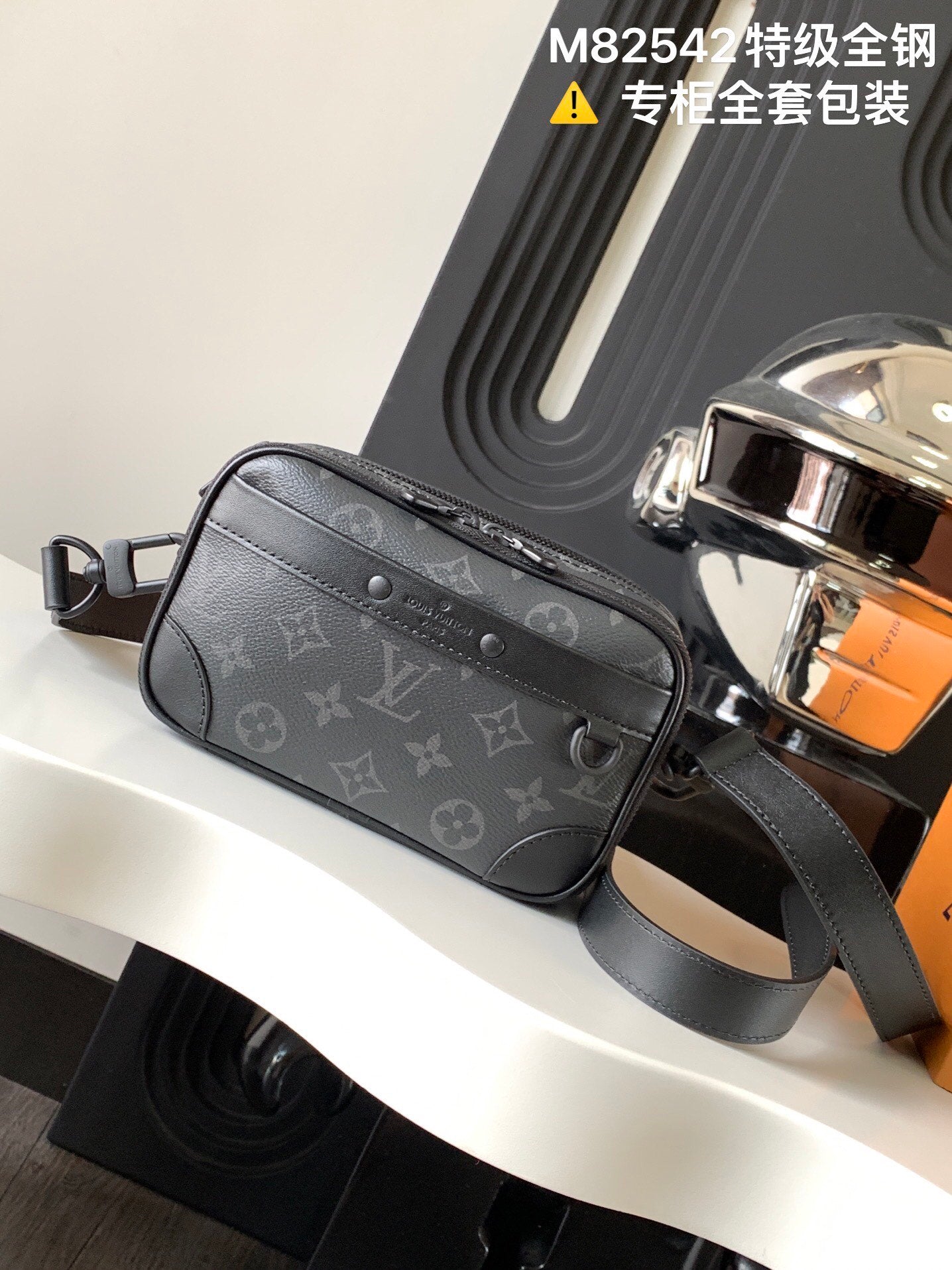 Crossbody bag with dark gray monogram canvas and top zipper, adjustable shoulder strap