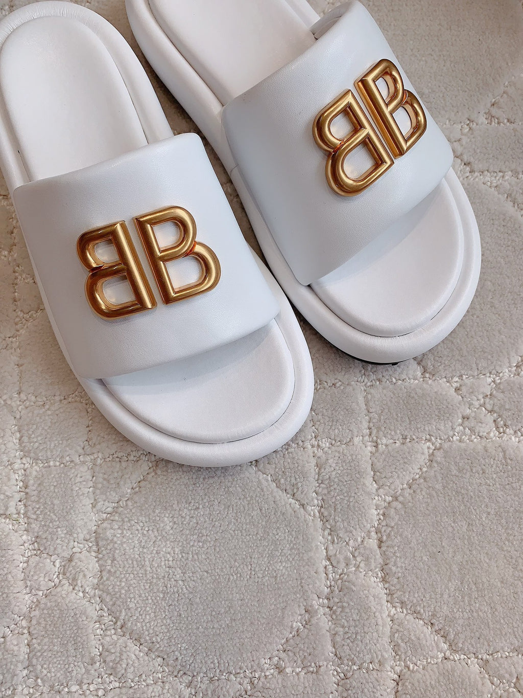 White slide sandals with gold BB buckle logo, close-up of straps