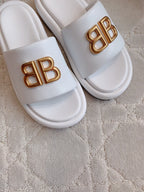 White slide sandals with gold BB buckle logo, close-up of straps