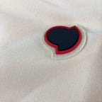 Close-up of red-and-navy heart logo patch on cream shorts fabric