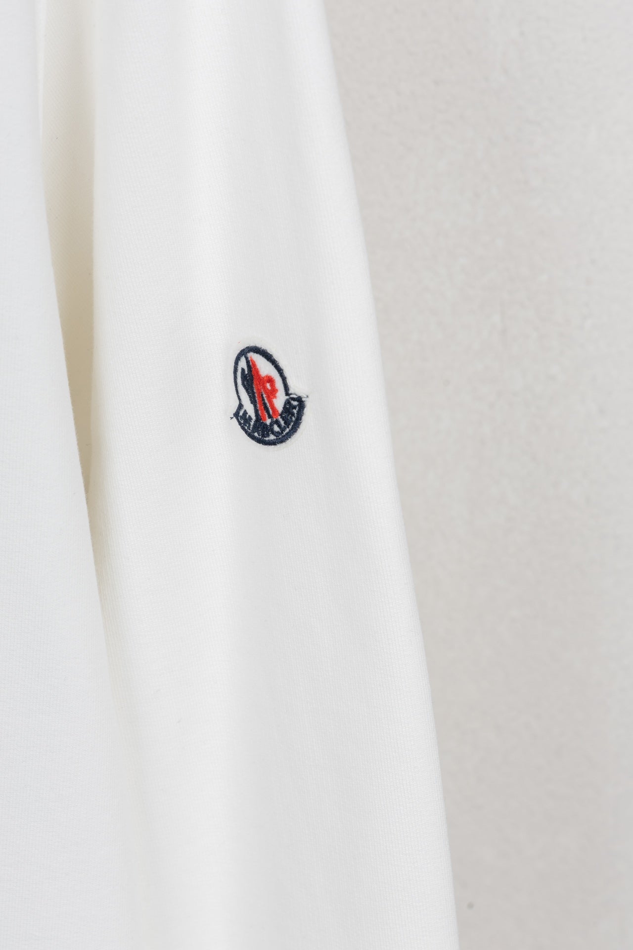 White sweatshirt sleeve with small embroidered logo patch