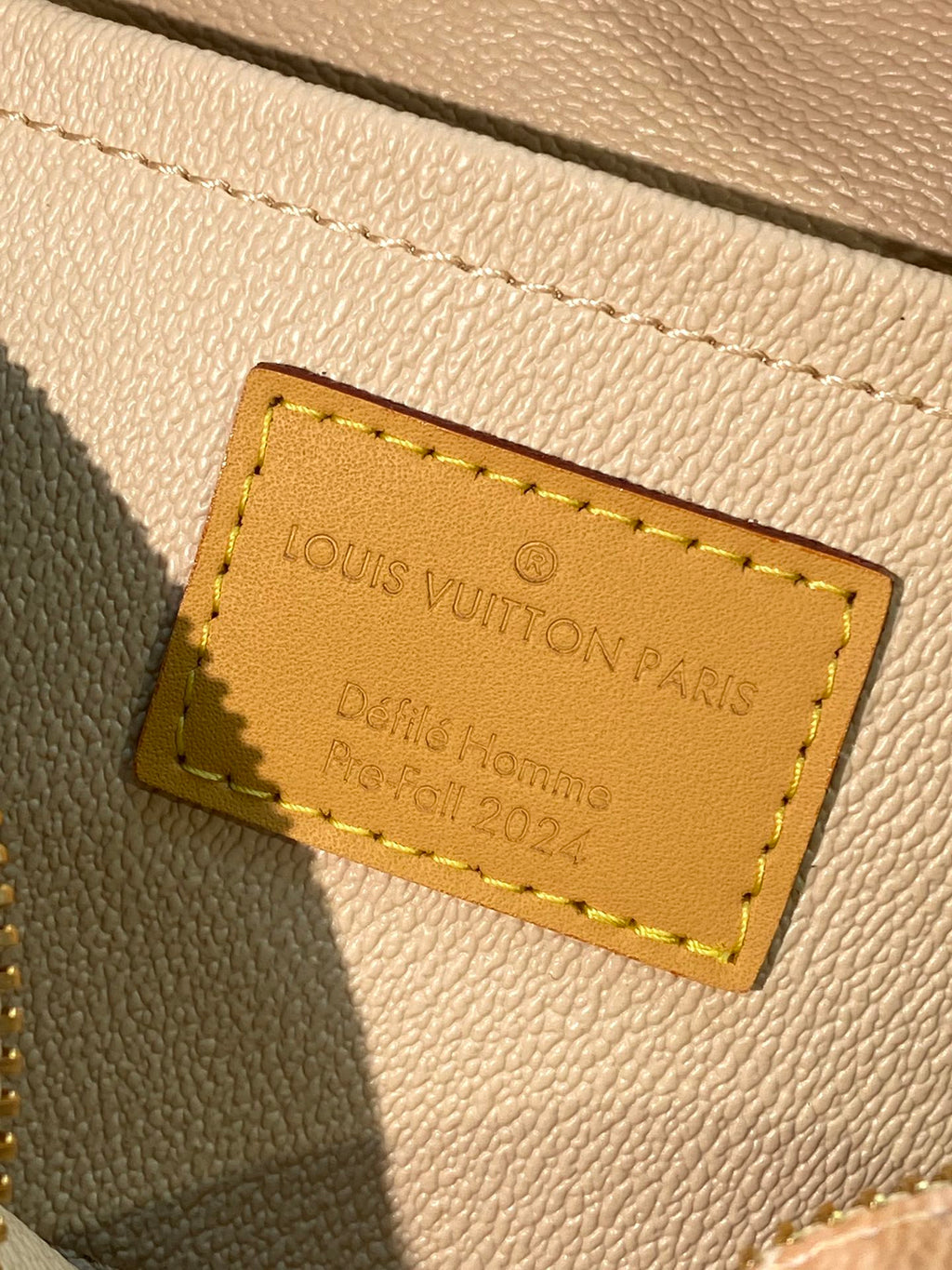 Louis Vuitton Paris leather label on bag front, gold logo text on beige.