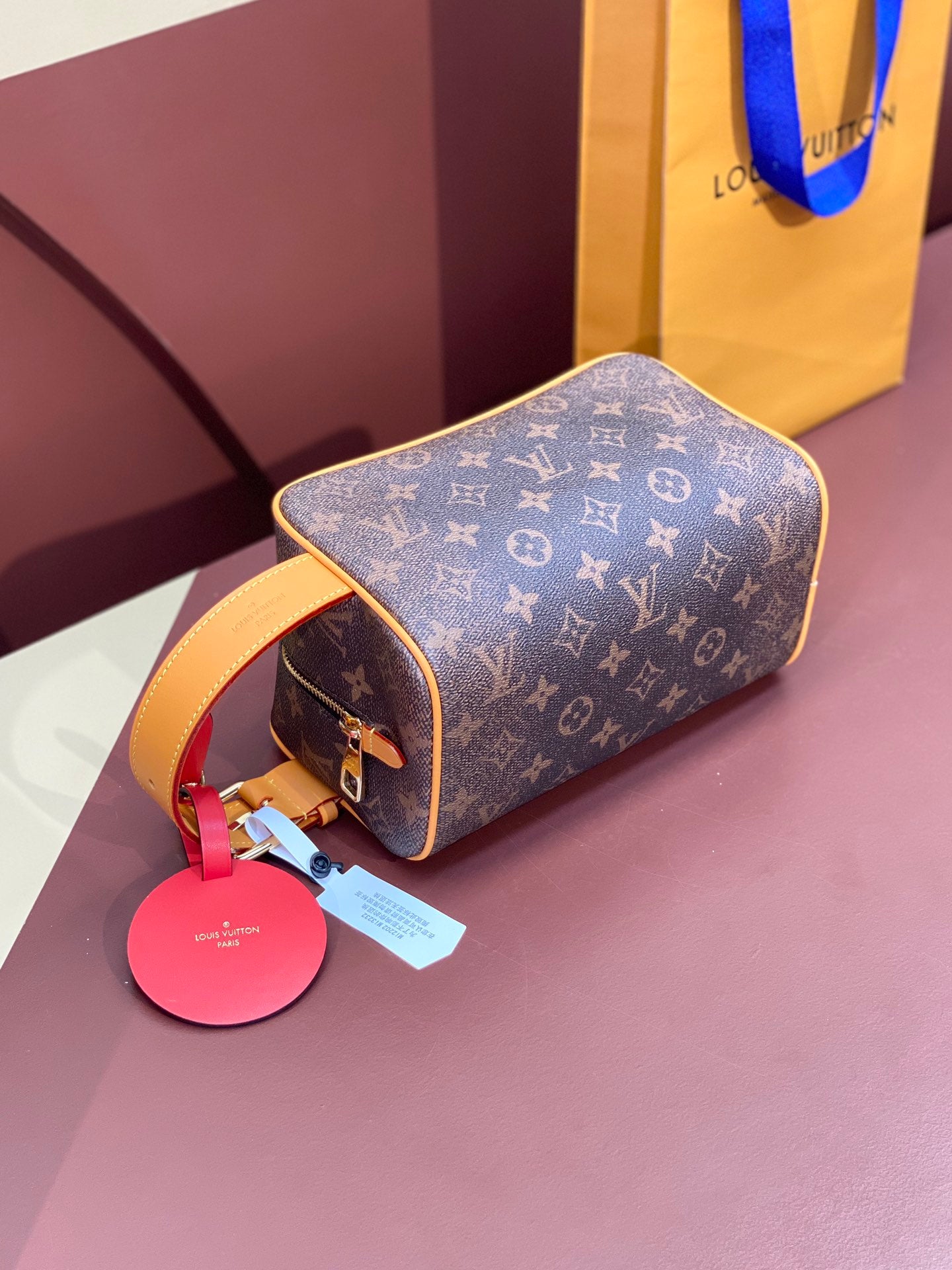 Louis Vuitton bag 3/4 view with tan handle, pink charm tag, and monogram canvas