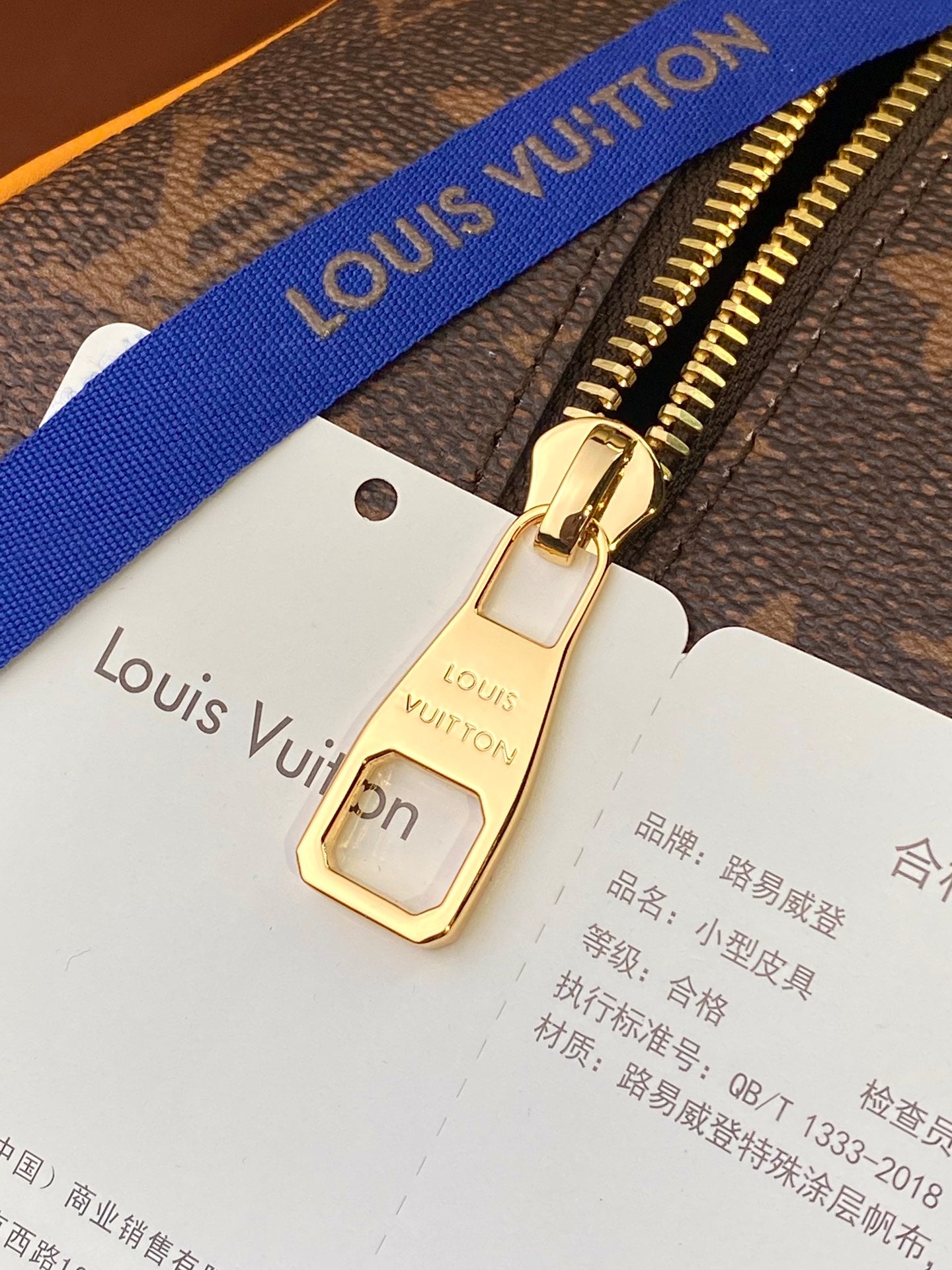 Louis Vuitton bag zipper pull with tan strap label card and blue webbing strap