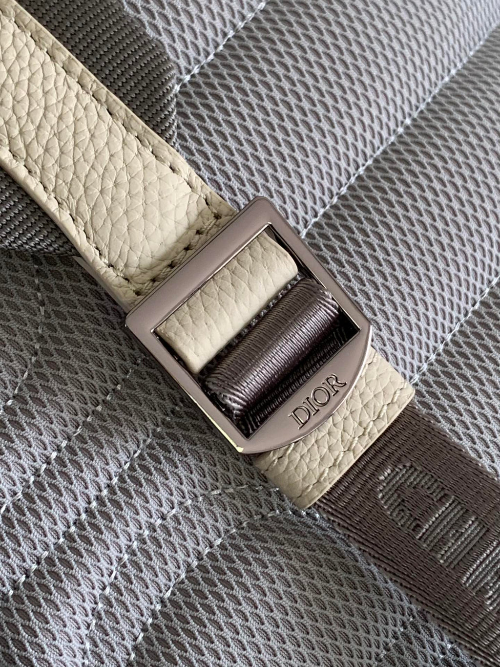 Cream backpack strap with Dior logo buckle and dark gray woven panel detail.