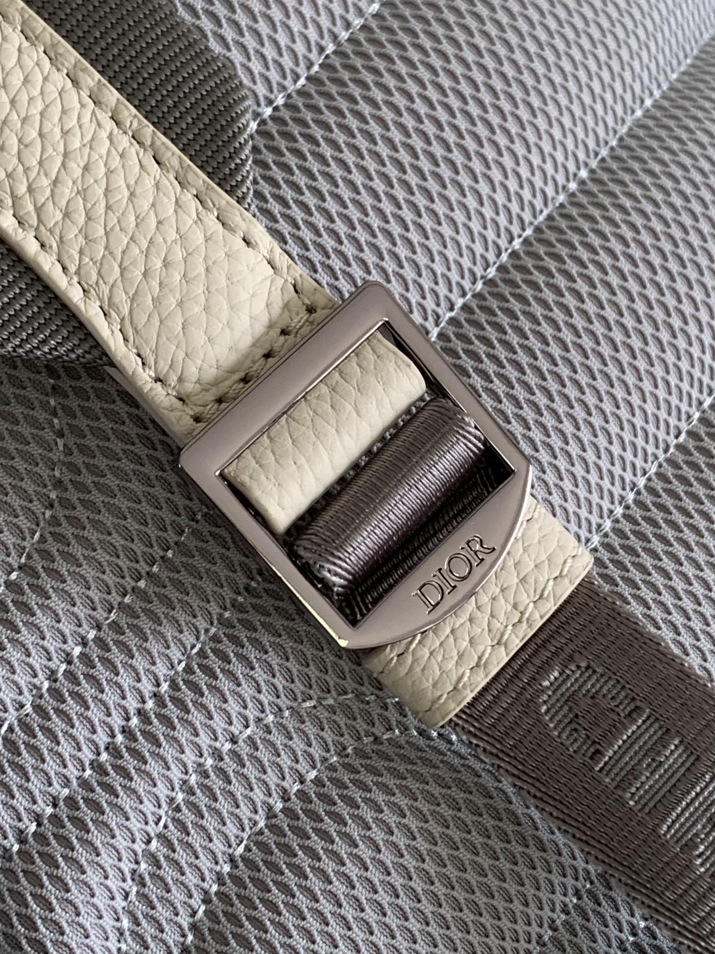 Cream backpack strap with Dior logo buckle and dark gray woven panel detail.
