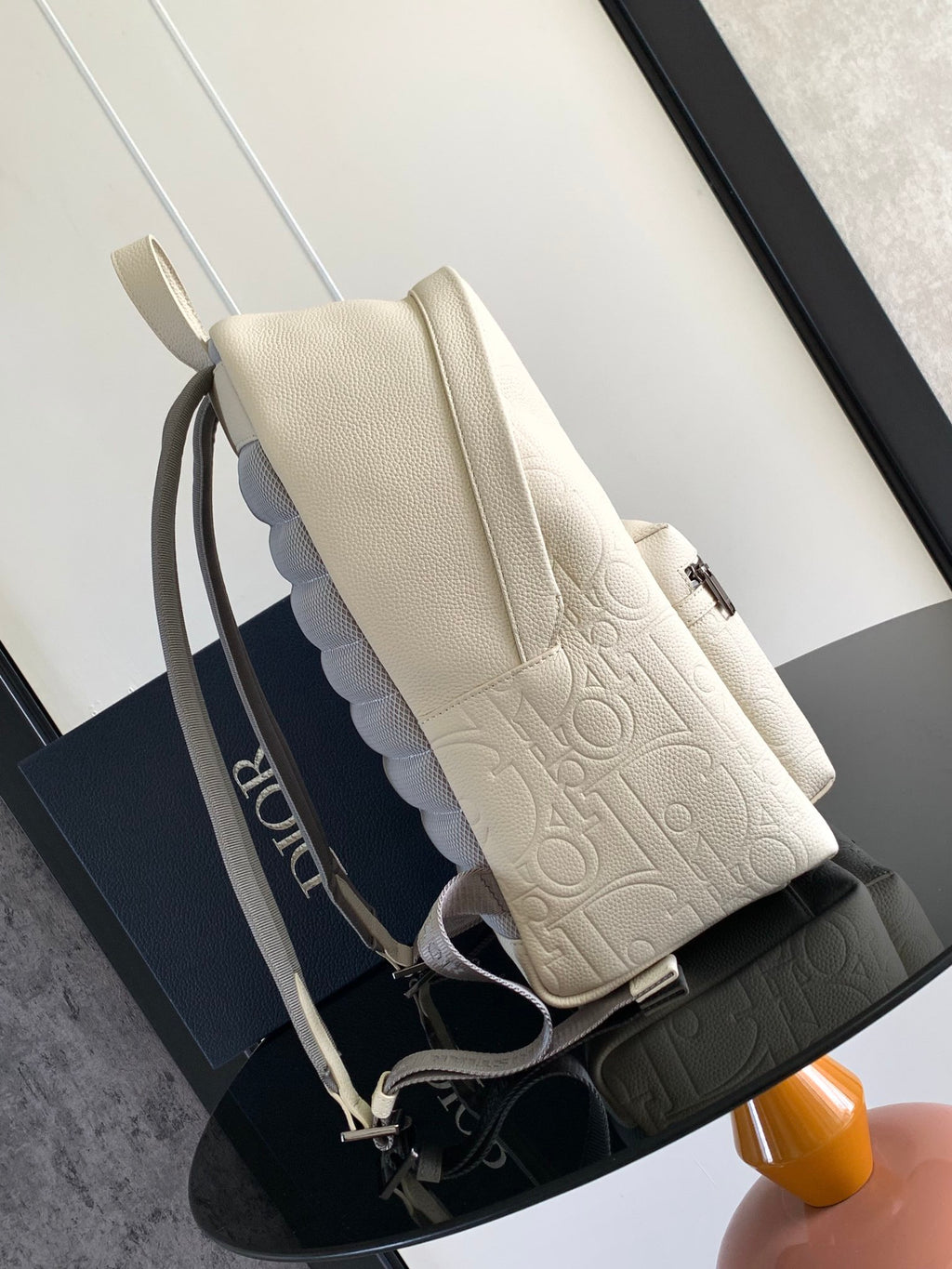 Cream embossed backpack with zip pocket, crossbody strap, and metal hardware.