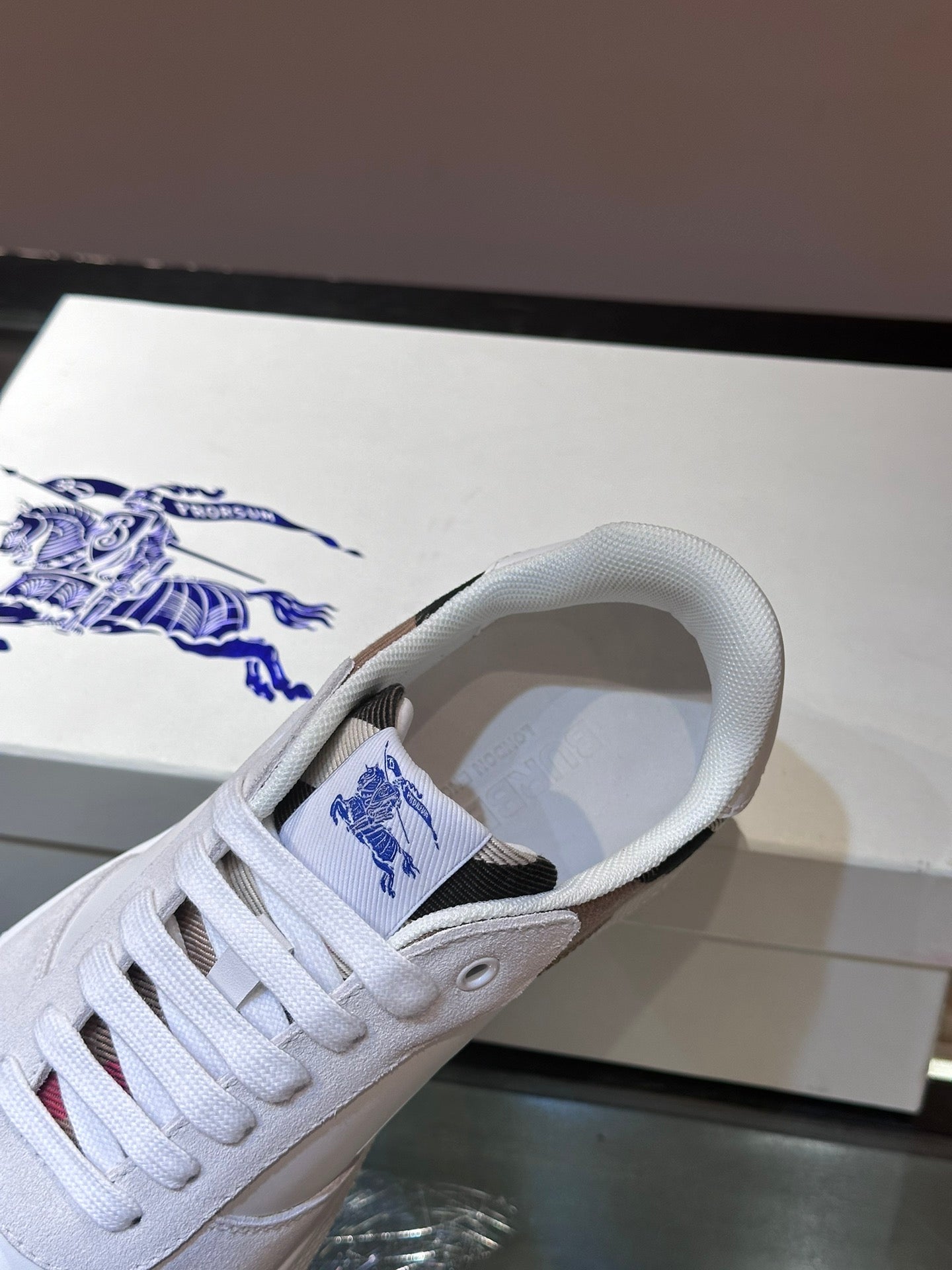Burberry white sneaker close-up with blue logo patch on tongue and lace eyelets
