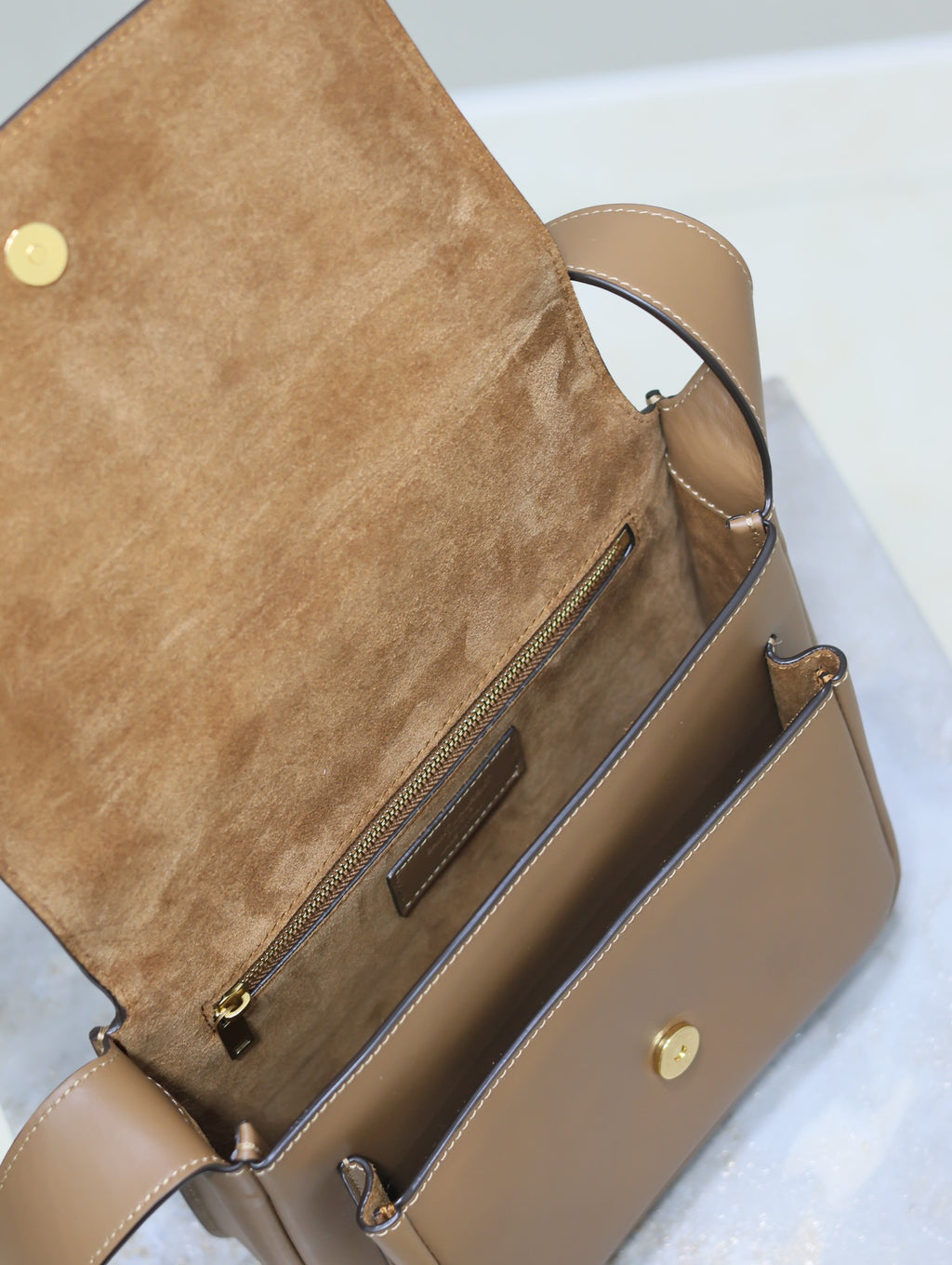 Tan leather flap bag interior view with zipper pocket and gold clasp