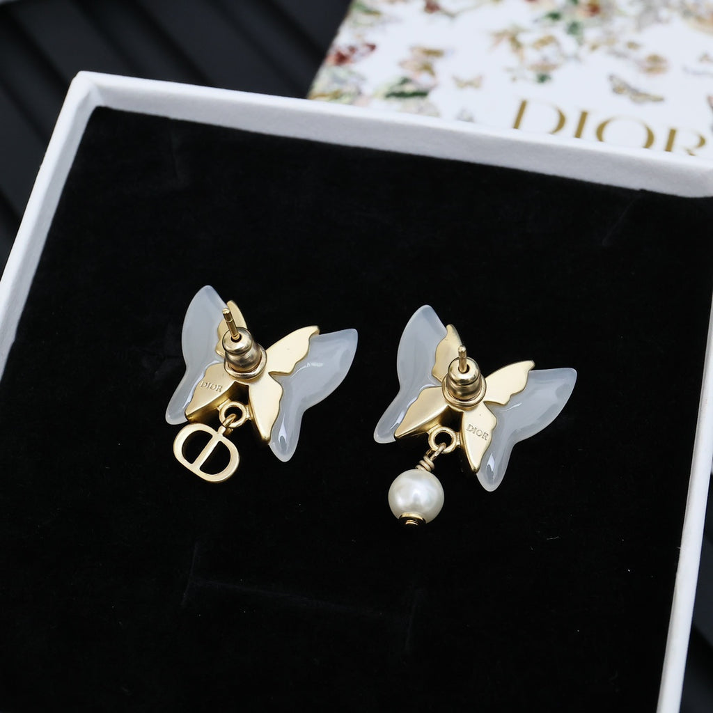 Gold-tone butterfly stud earrings with faux pearl dangles on black card