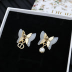 Gold-tone butterfly stud earrings with faux pearl dangles on black card