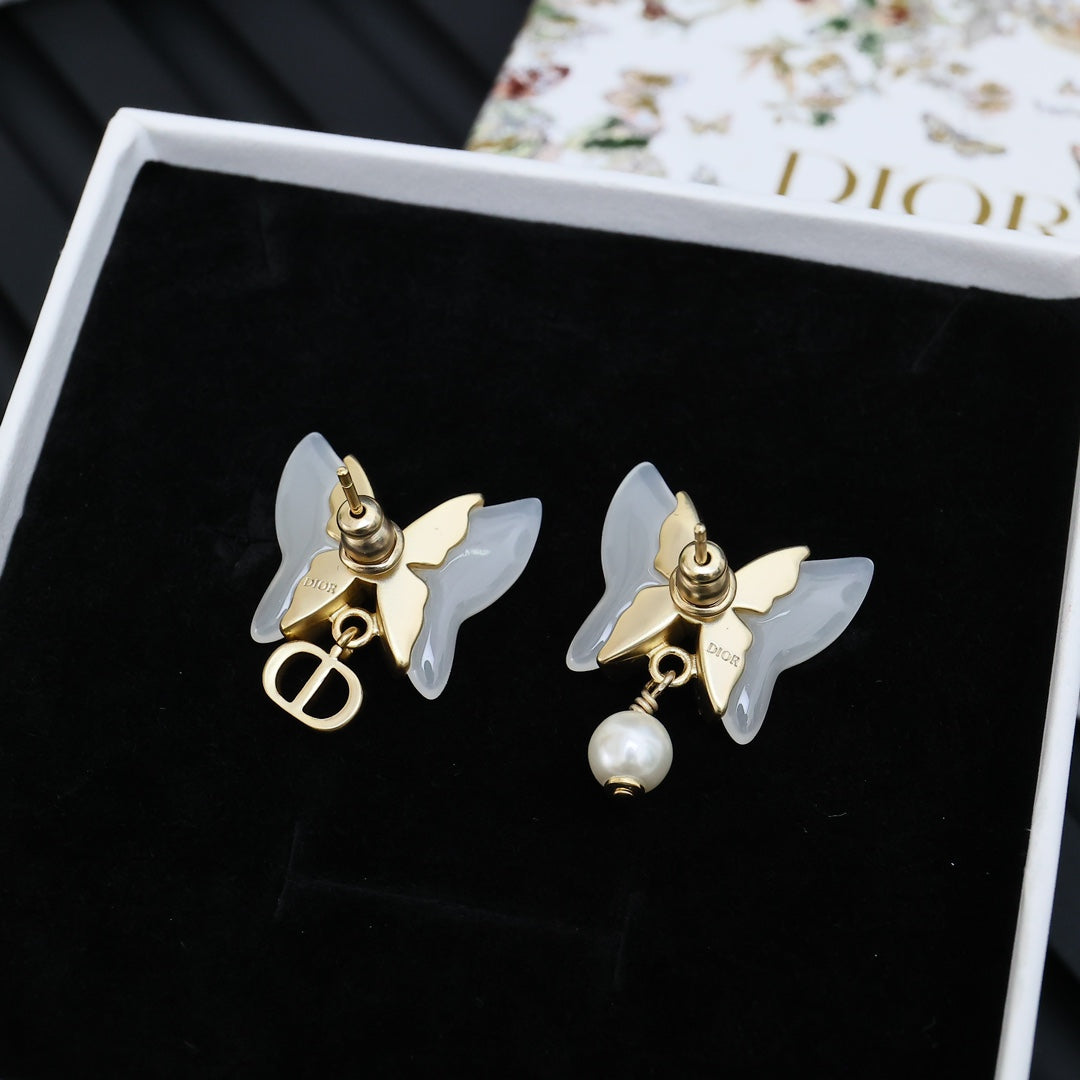 Gold-tone butterfly stud earrings with faux pearl dangles on black card