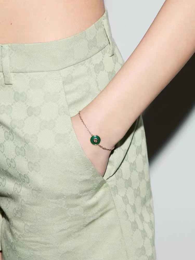 Bracelet on wrist with gold chain and round green enamel charm