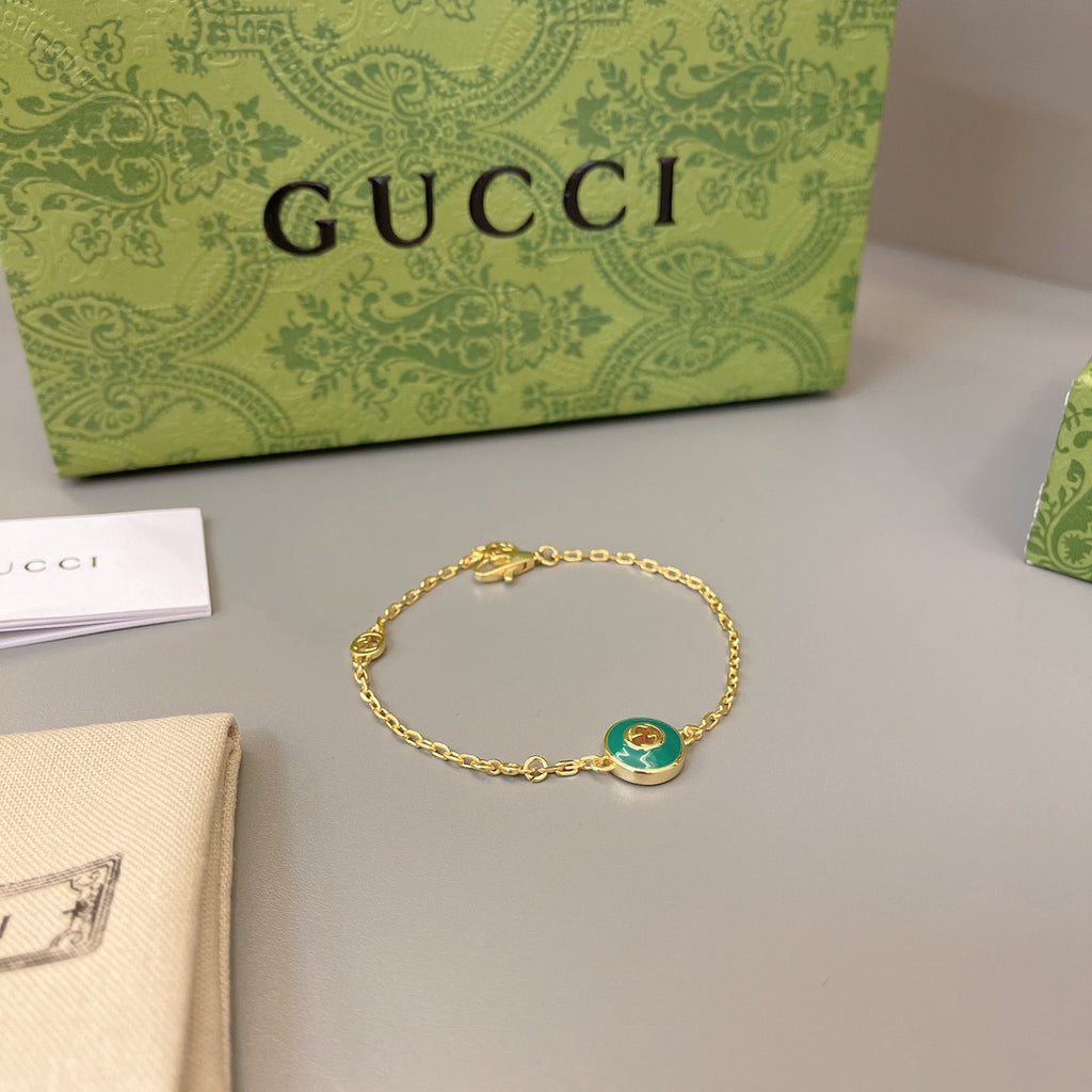 Gold chain bracelet with round green enamel charm and small dangling detail
