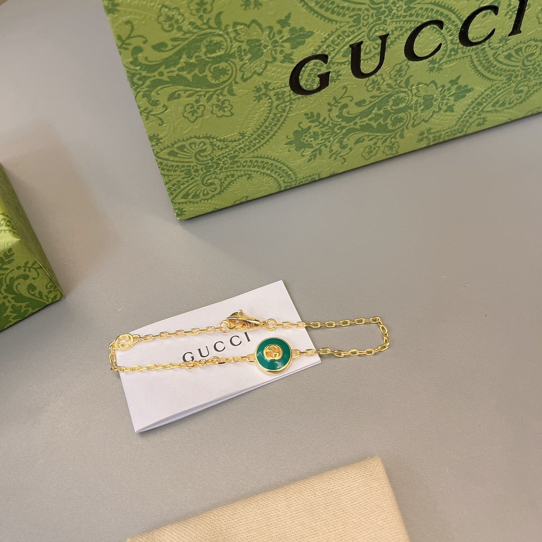 Gold bracelet with green enamel round charm and white tag with Gucci print
