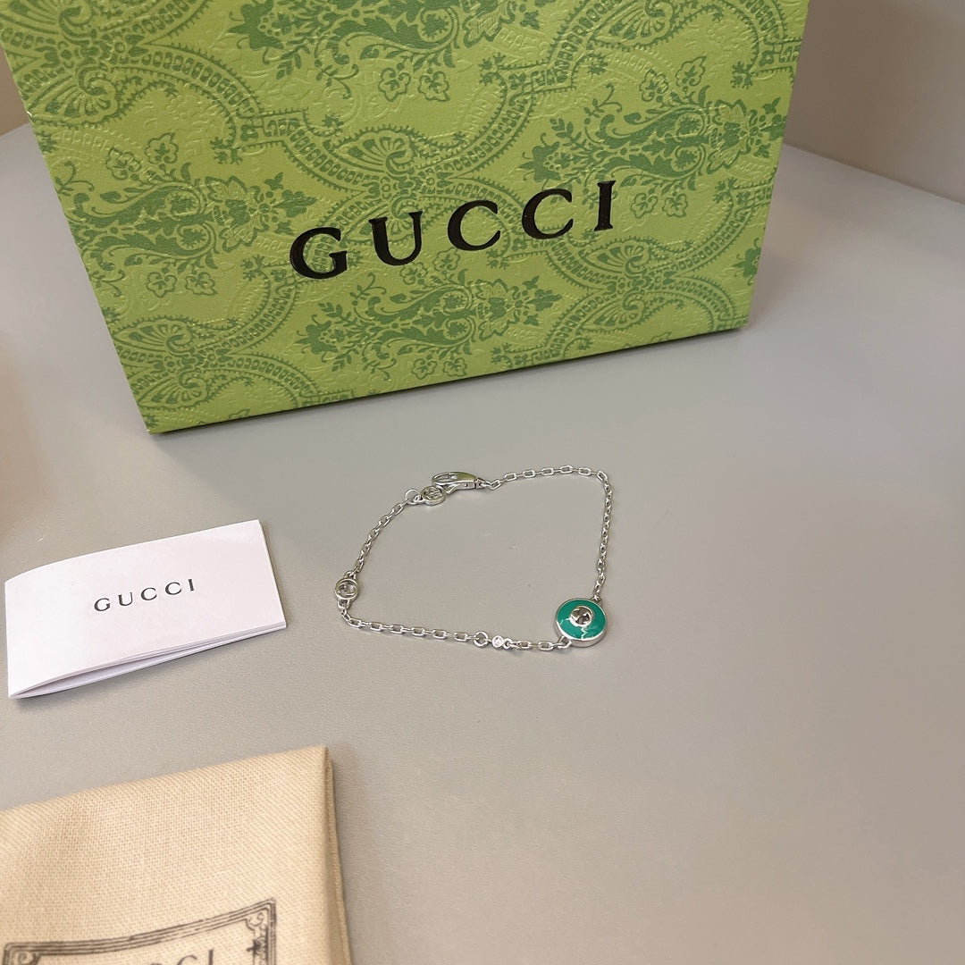 Gucci silver bracelet with green enamel charm beside dust bag and box