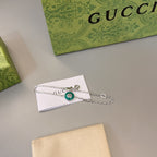 Gucci silver bracelet with circular green charm, resting on a white card